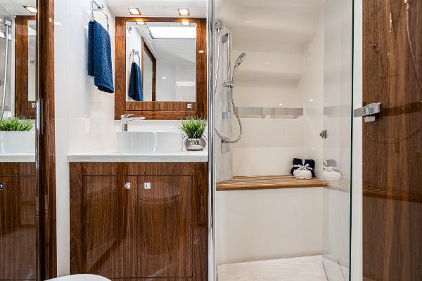 Luxurious bathroom in 2021 Riviera 5400 Sport Yacht with wooden cabinetry and glass shower.