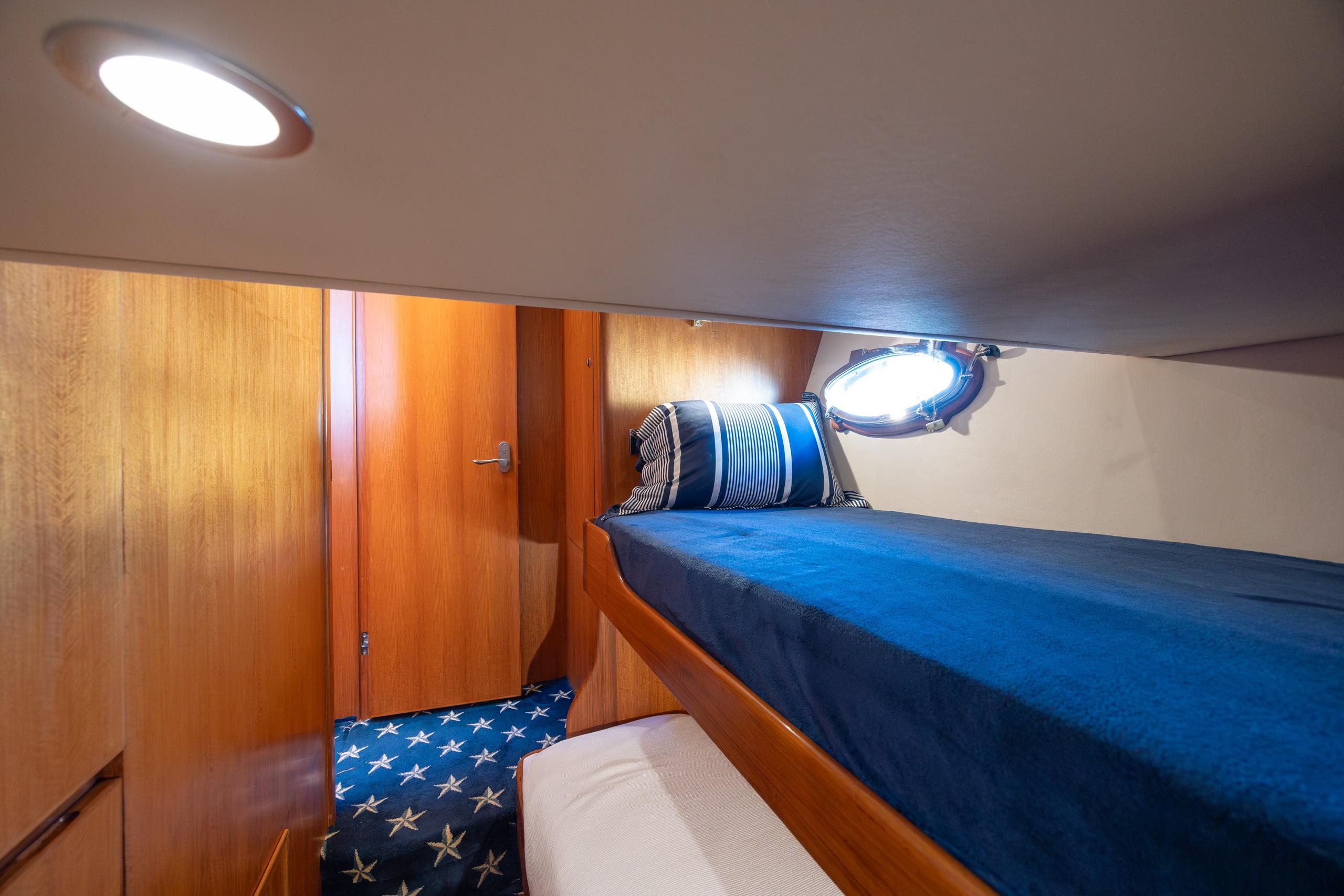 Cozy cabin interior of 2005 Ocean Alexander 52 Sedan yacht with blue bedding and wooden accents.
