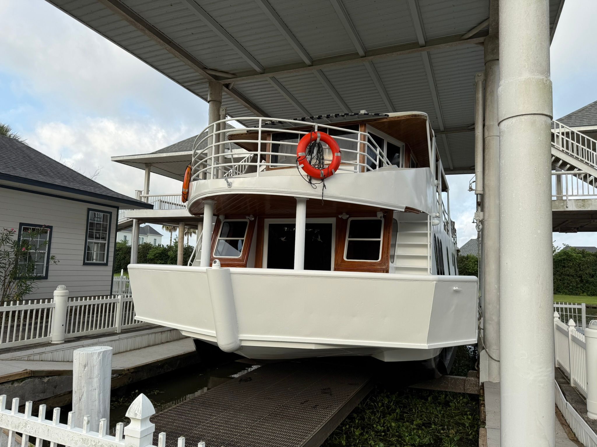 A white houseboat with a red lifebuoy, situated in a covered area.