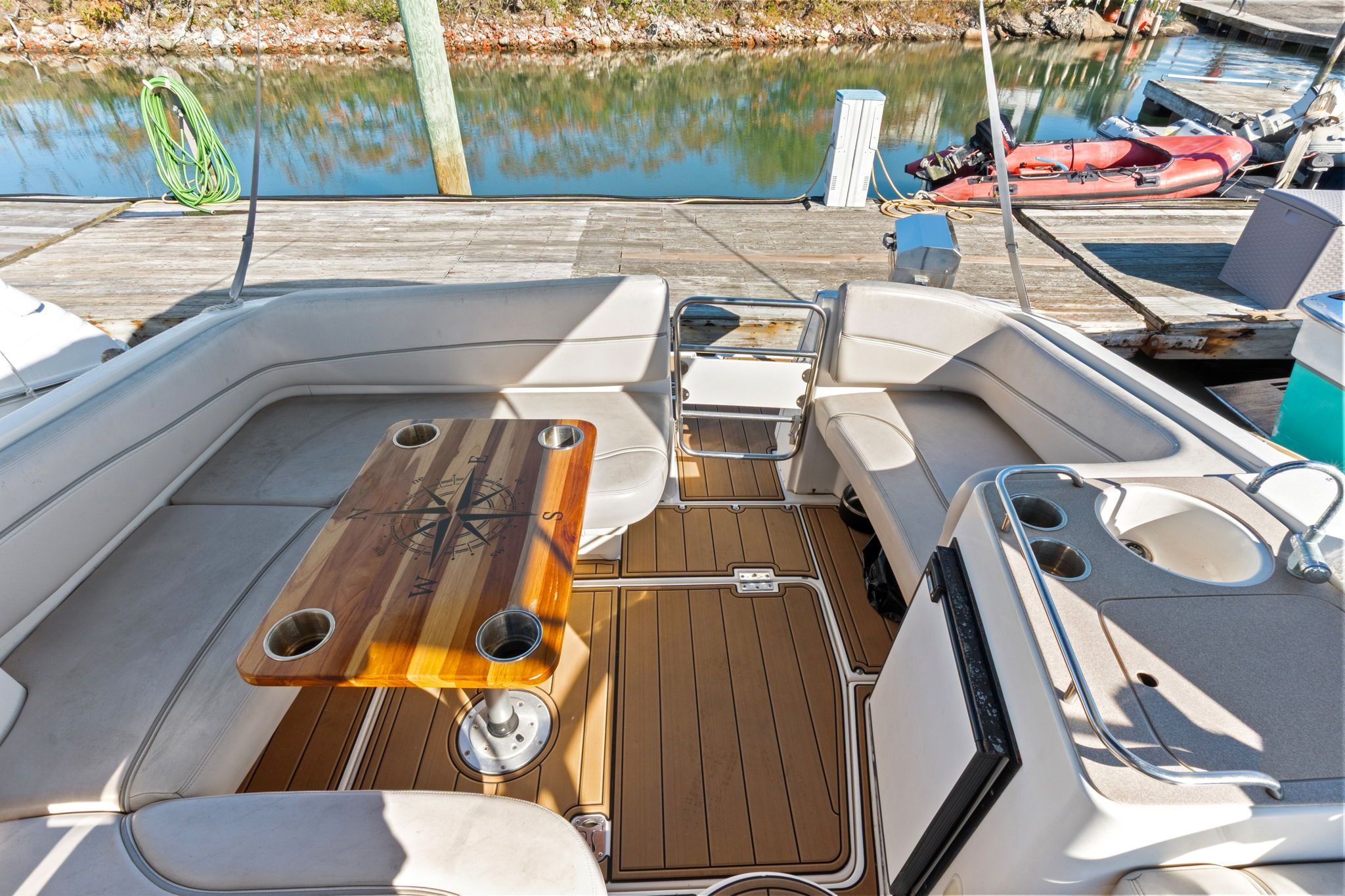 The image shows the cockpit of a 2007 Larson Cabrio 330. It features U-shaped seating and a wooden table with a compass design. The flooring is teak, and there's a small kitchenette with a sink.