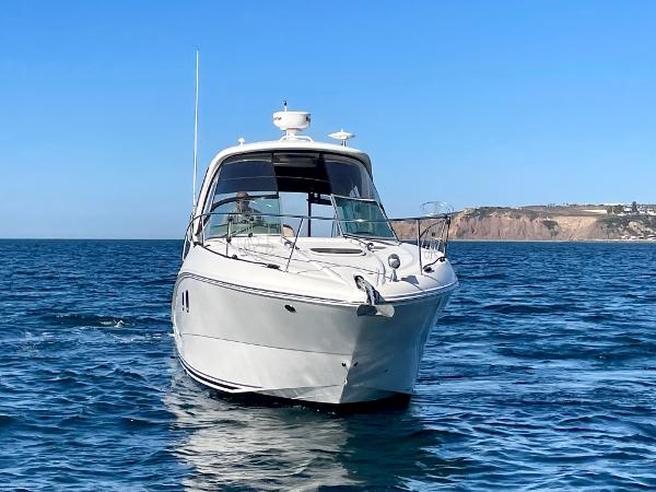 2014 Sea Ray 330 Sundancer cruising on open water with coastal cliffs in the background.
