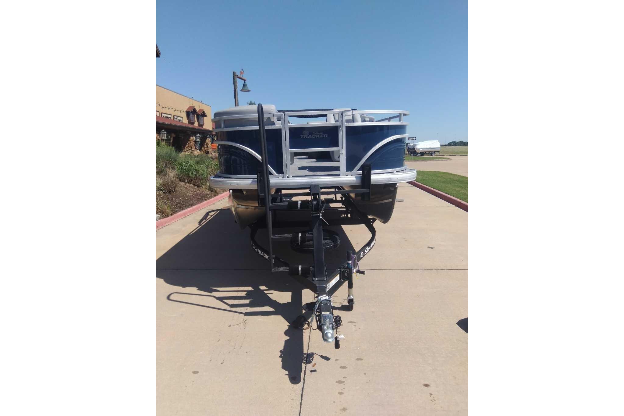 2026 Sun Tracker SportFish 20 DLX pontoon boat on trailer, parked outdoors.