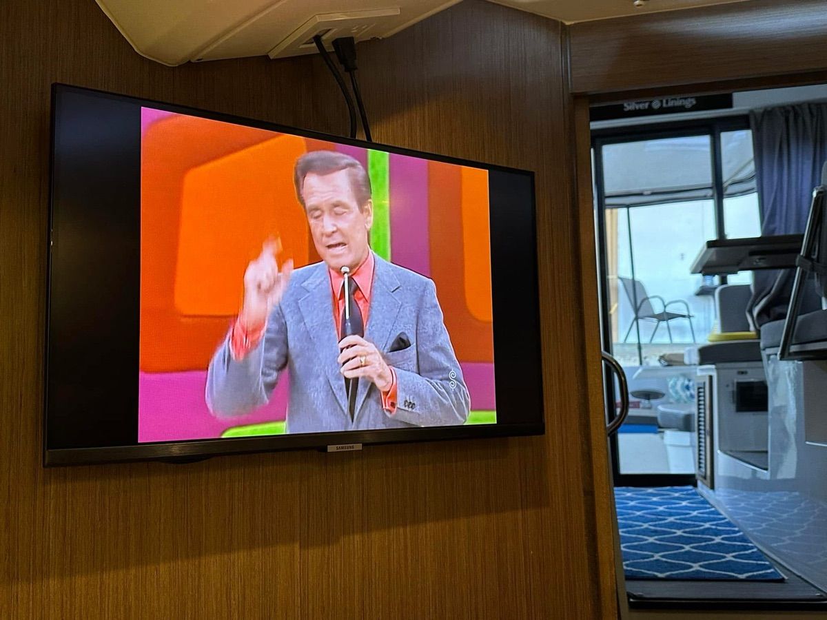 A TV displays a game show in a modern boat interior.