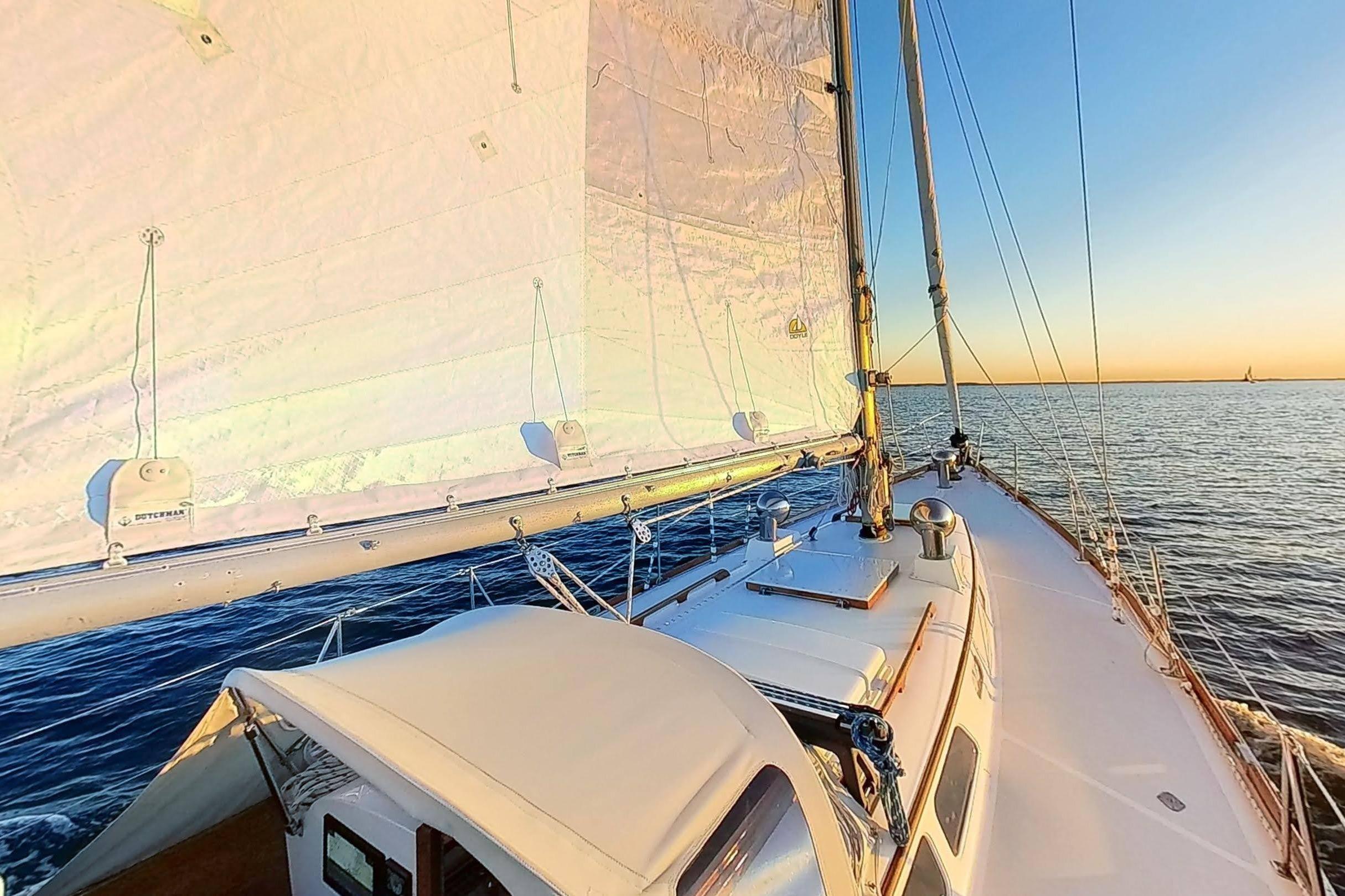 Sailing on a 1970 Hinckley Bermuda 40 yacht at sunset over calm waters.