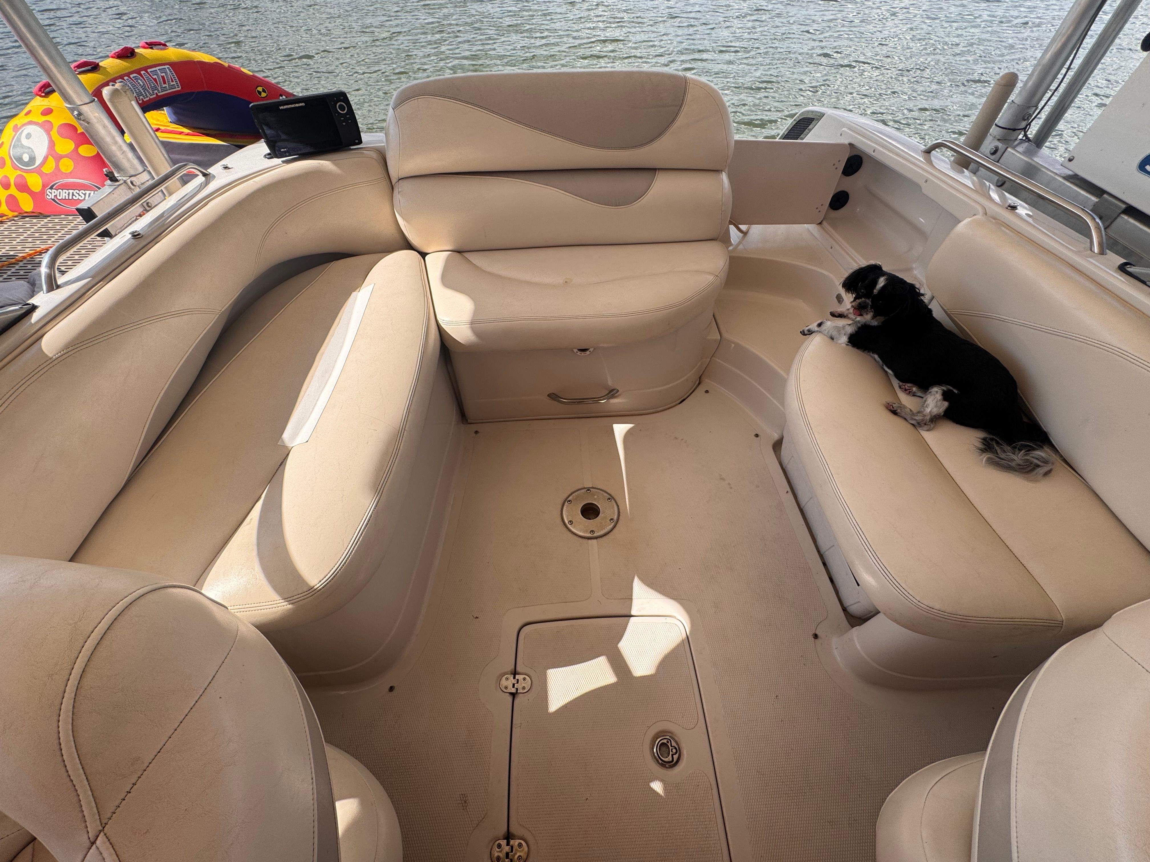 A dog lies on a bench in a boat with beige upholstery, surrounded by water.