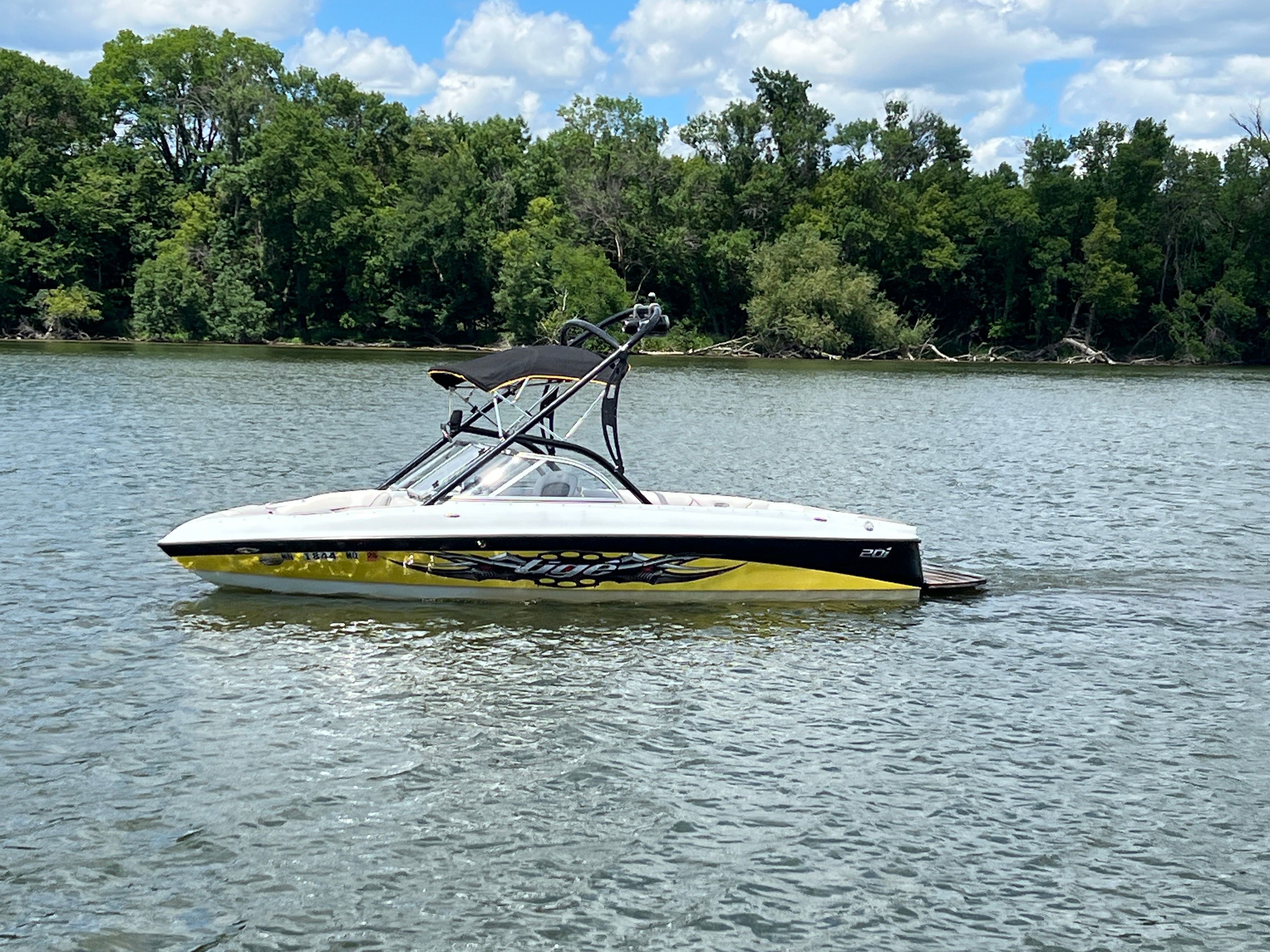 A 2006 Tigé 20i boat on a calm river, surrounded by lush trees.