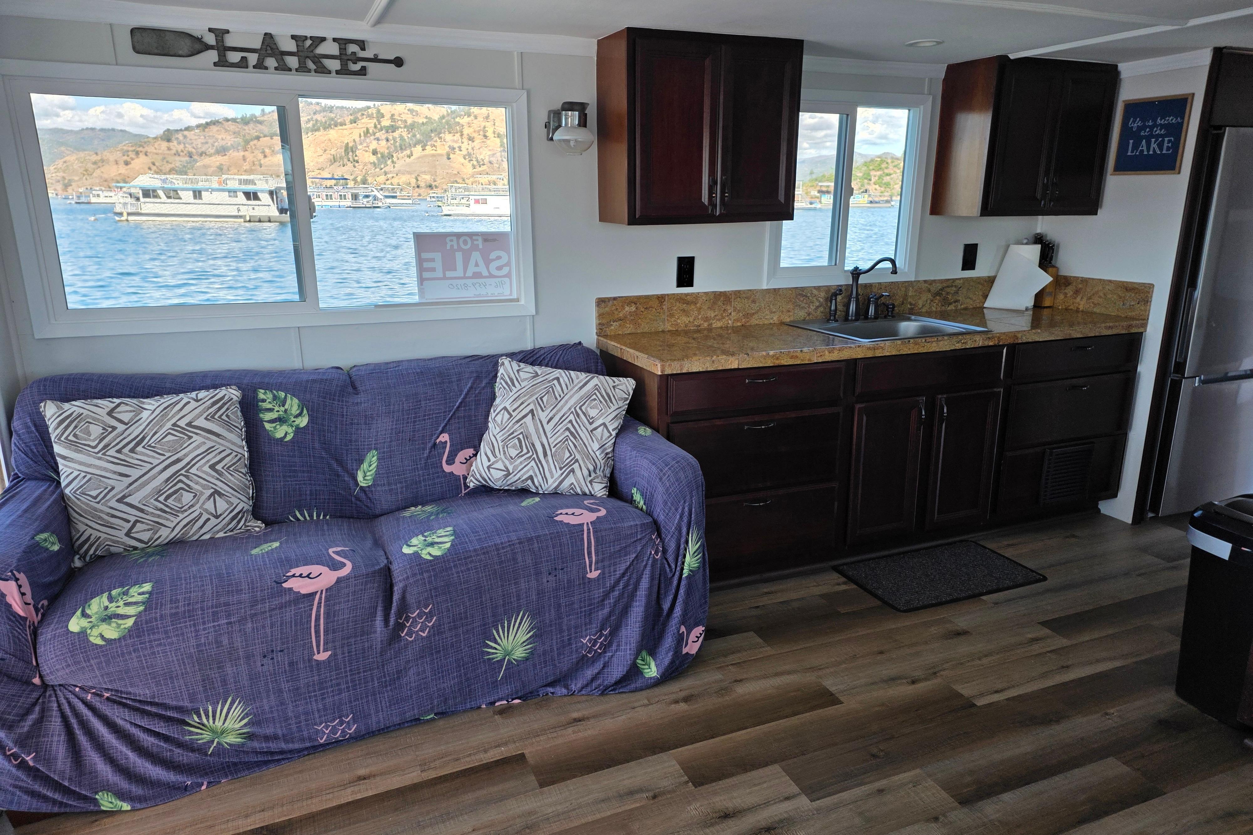 Interior of a 2007 custom houseboat with cozy seating and kitchen area, overlooking a scenic lake.