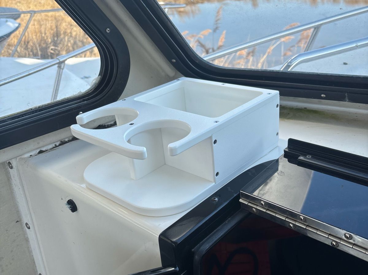 A white cup holder is mounted on a boat's dashboard. Water is visible outside.
