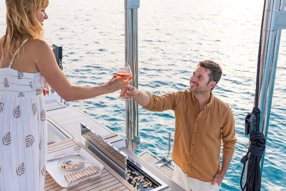 Couple enjoying drinks on a 2026 Dufour 48 yacht, with ocean backdrop.