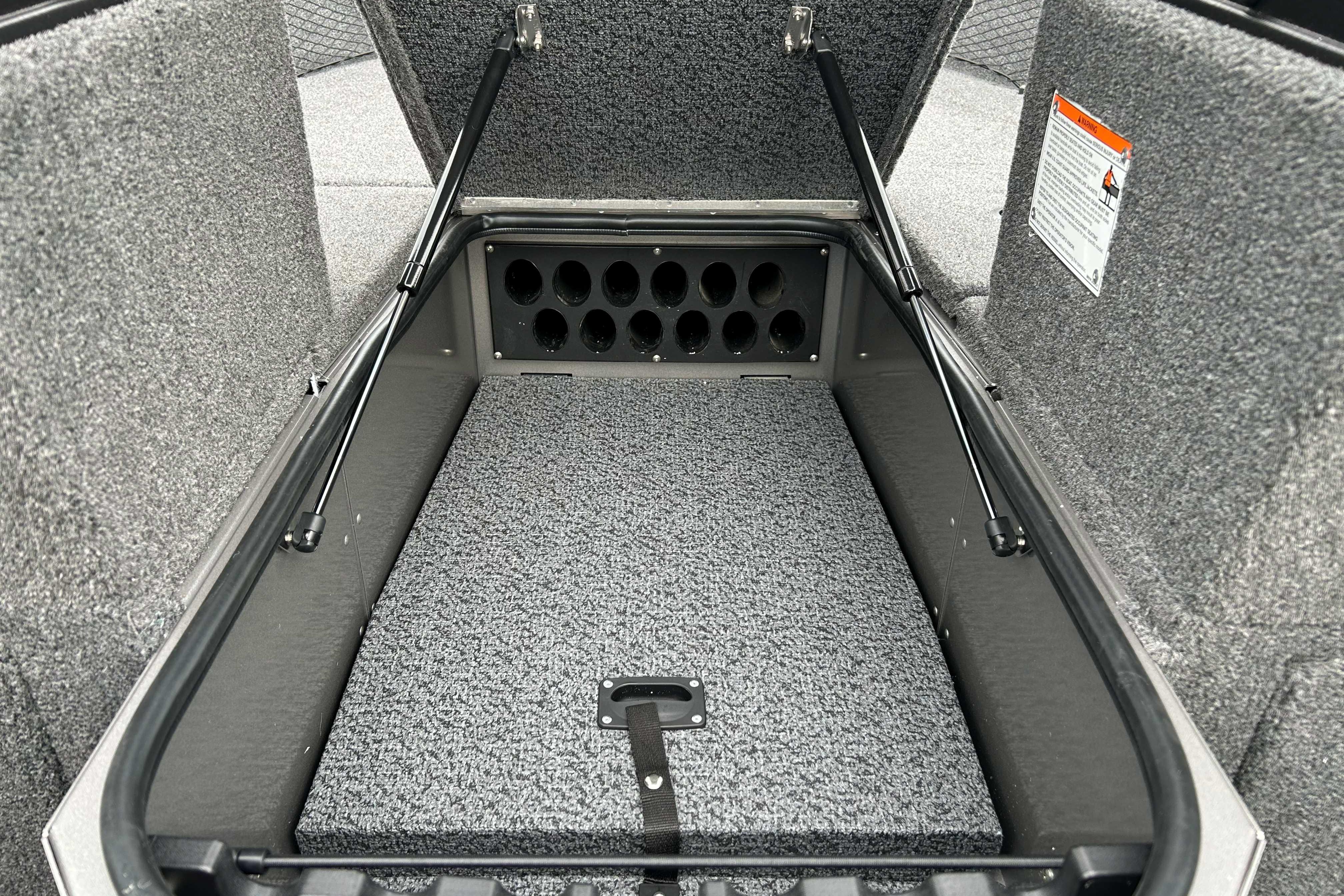 Open storage compartment in 2027 Lund 1775 Impact XS boat, featuring rod holders and carpeted interior.