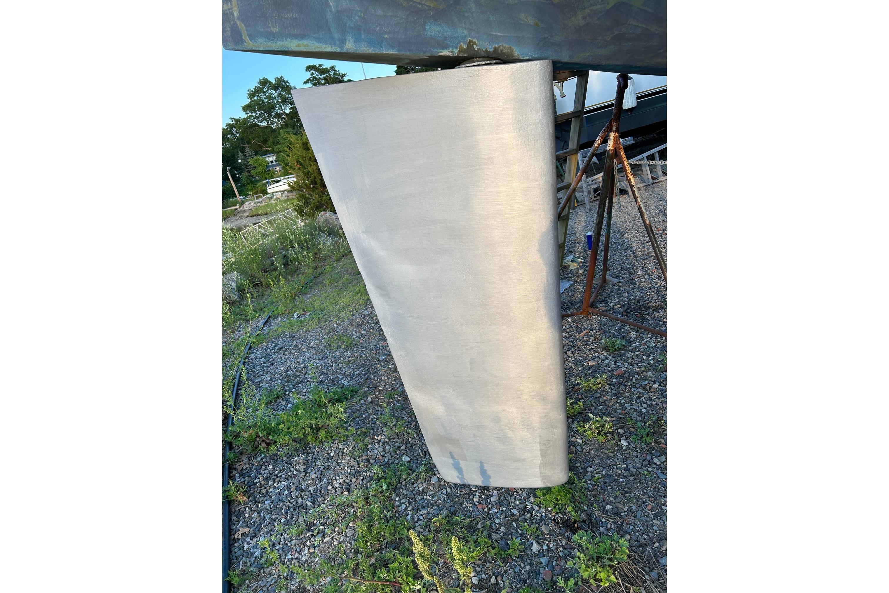 Keel of 1987 Ericson 38-200 sailboat on gravel with greenery in background.