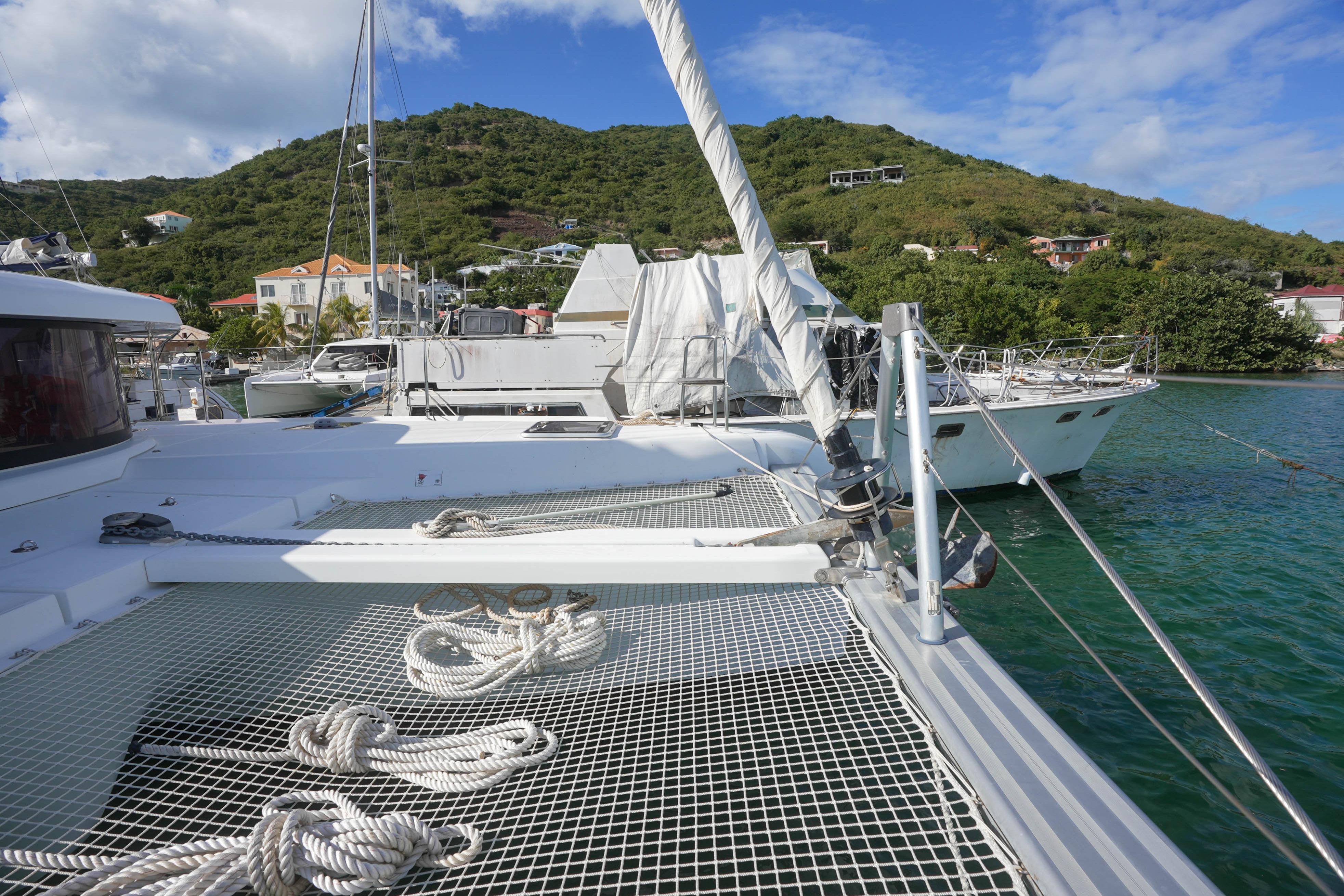 Catamaran Lagoon 42, 2019 model, docked in scenic marina with lush hillside backdrop.