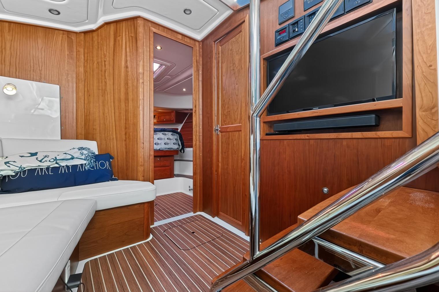 Luxurious lower deck seating/TV area of 2024 Back Cove 39O yacht with wood paneling, owners stateroom entrance and day head entrance.