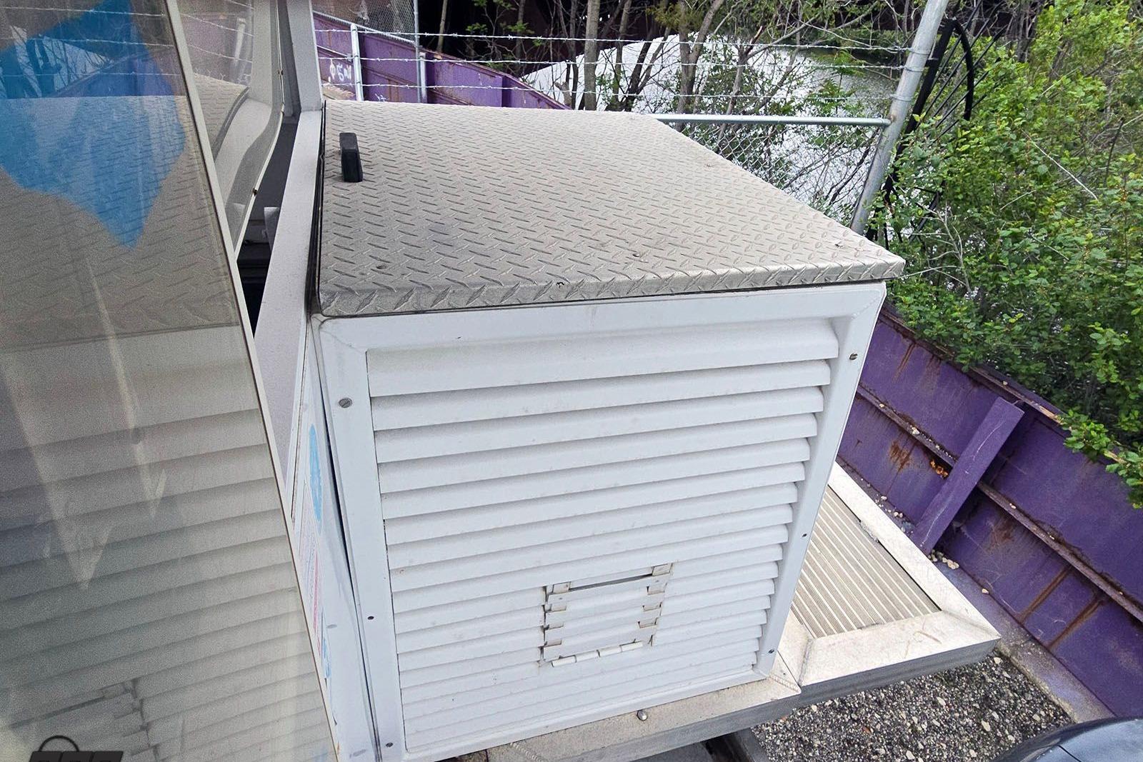2008 Trident 5012 Pontoon with metal storage compartment, surrounded by greenery and fencing.