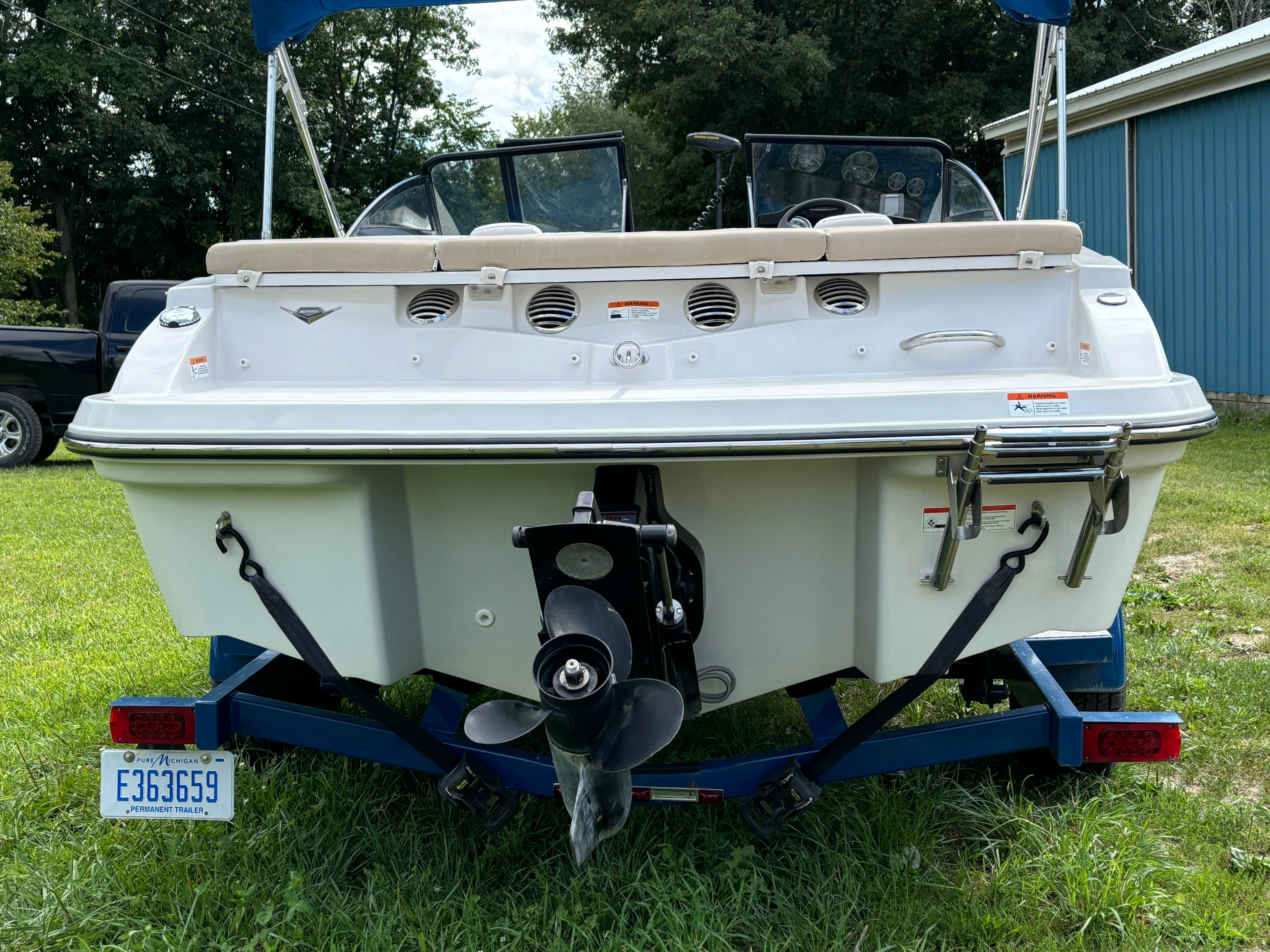 Rear view of a Glastron GTSF 185 boat on a trailer, parked on grass.