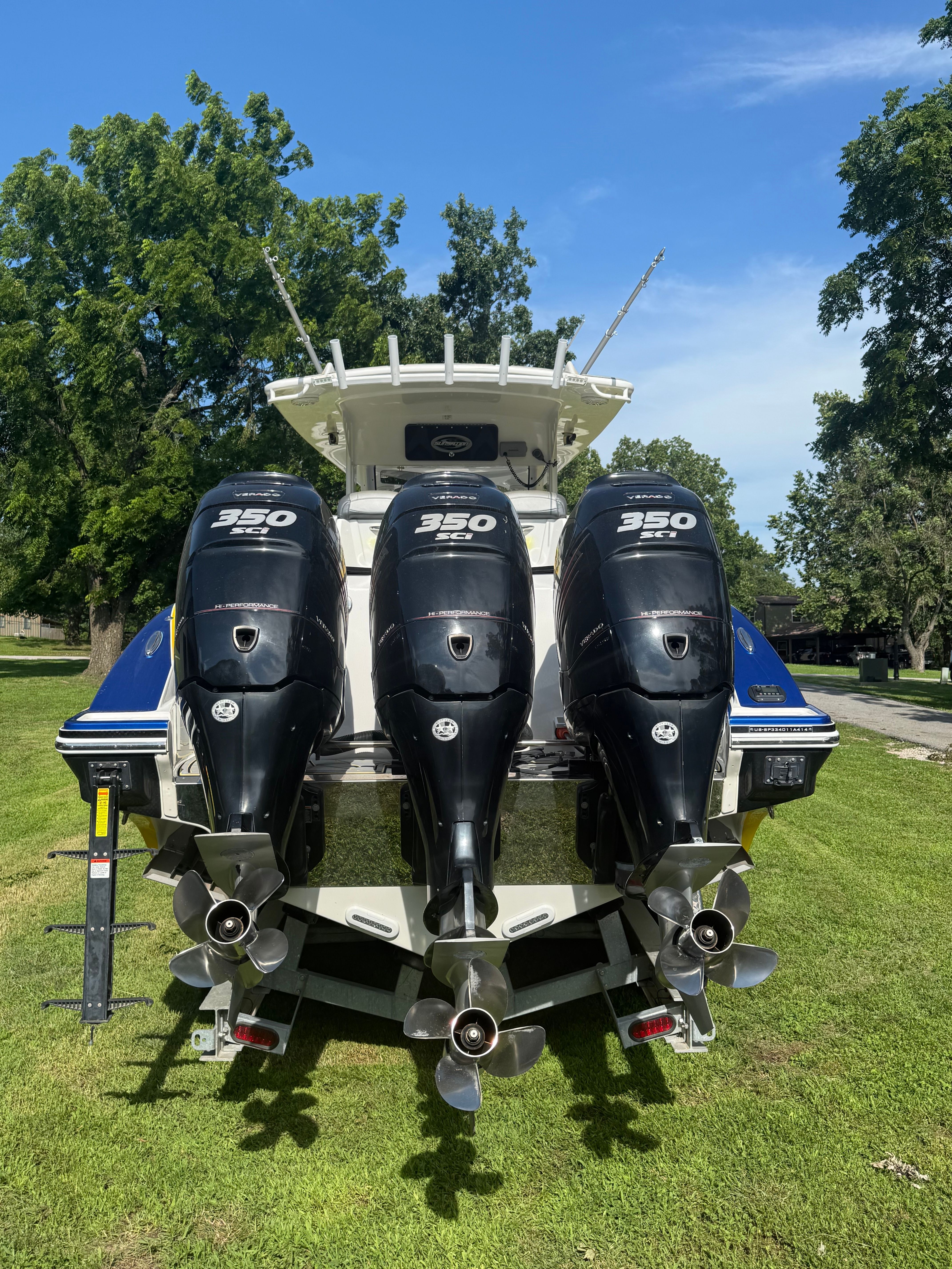 Triple-engine boat on grass, featuring a blue hull and trees in the background.