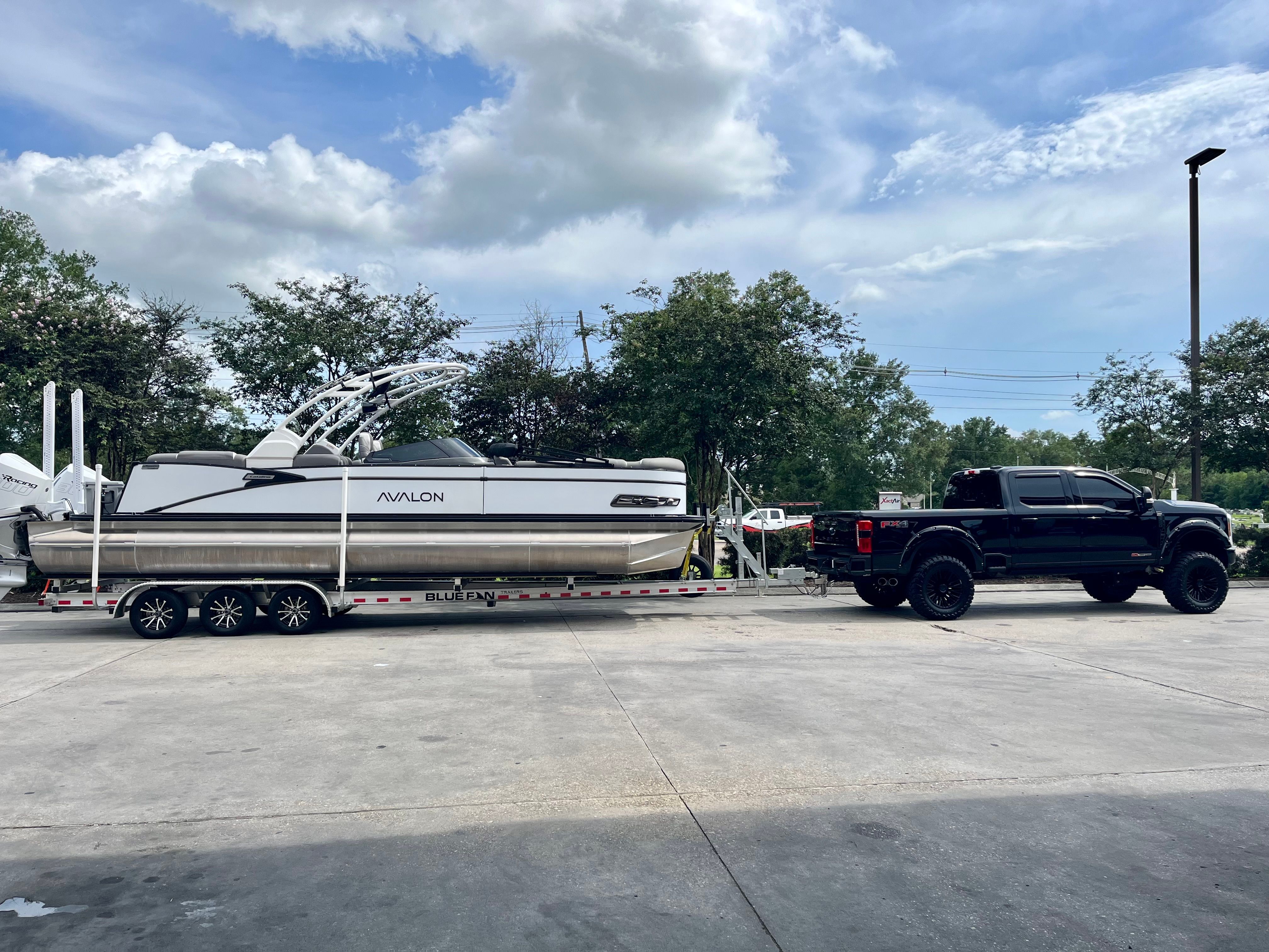 A 2024 Avalon Catalina Quad Lounger on a trailer, towed by a black pickup truck.