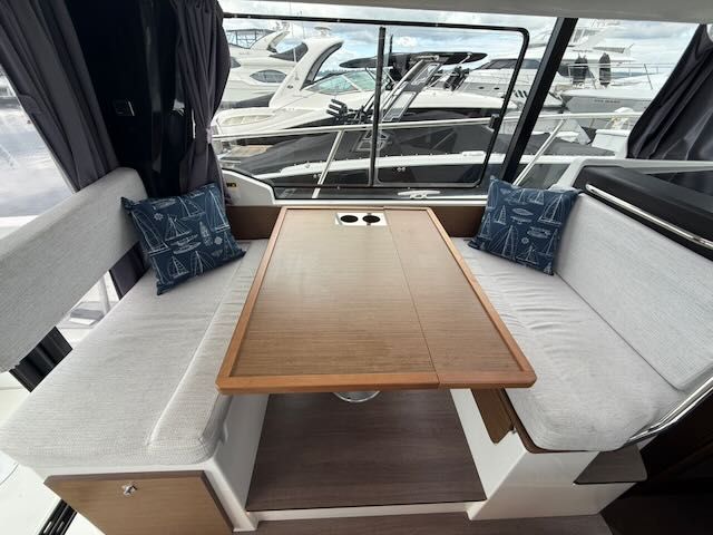 Interior view of a Jeanneau NC 1095 with a wooden table and white benches.