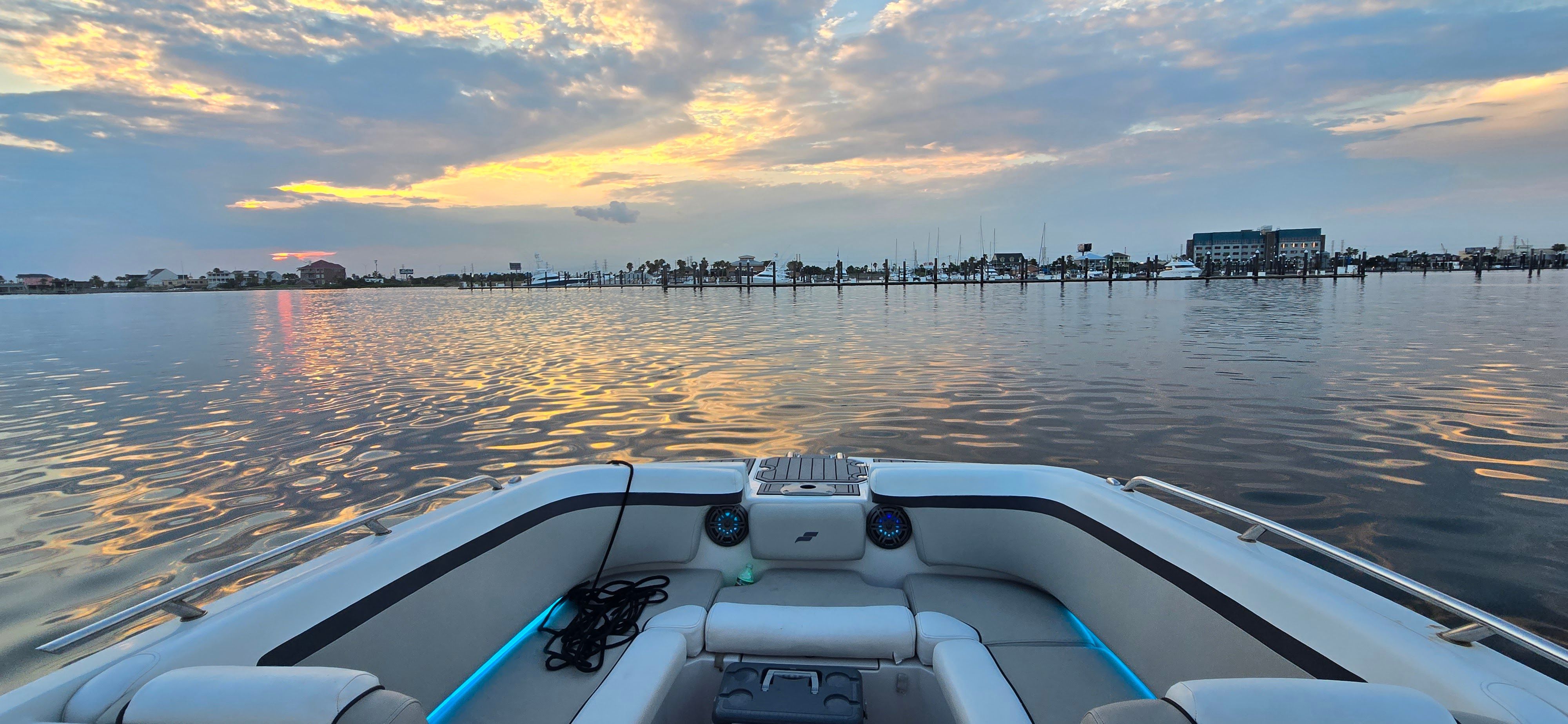 A boat on calm water at sunset, overlooking a harbor.