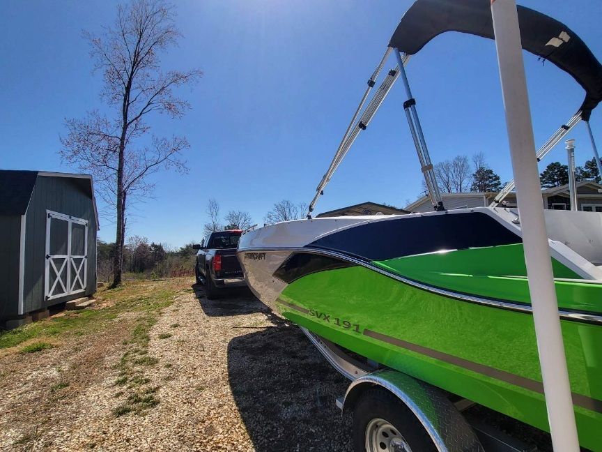 A green 2023 Starcraft SVX 191 OB boat on a trailer next to a shed.