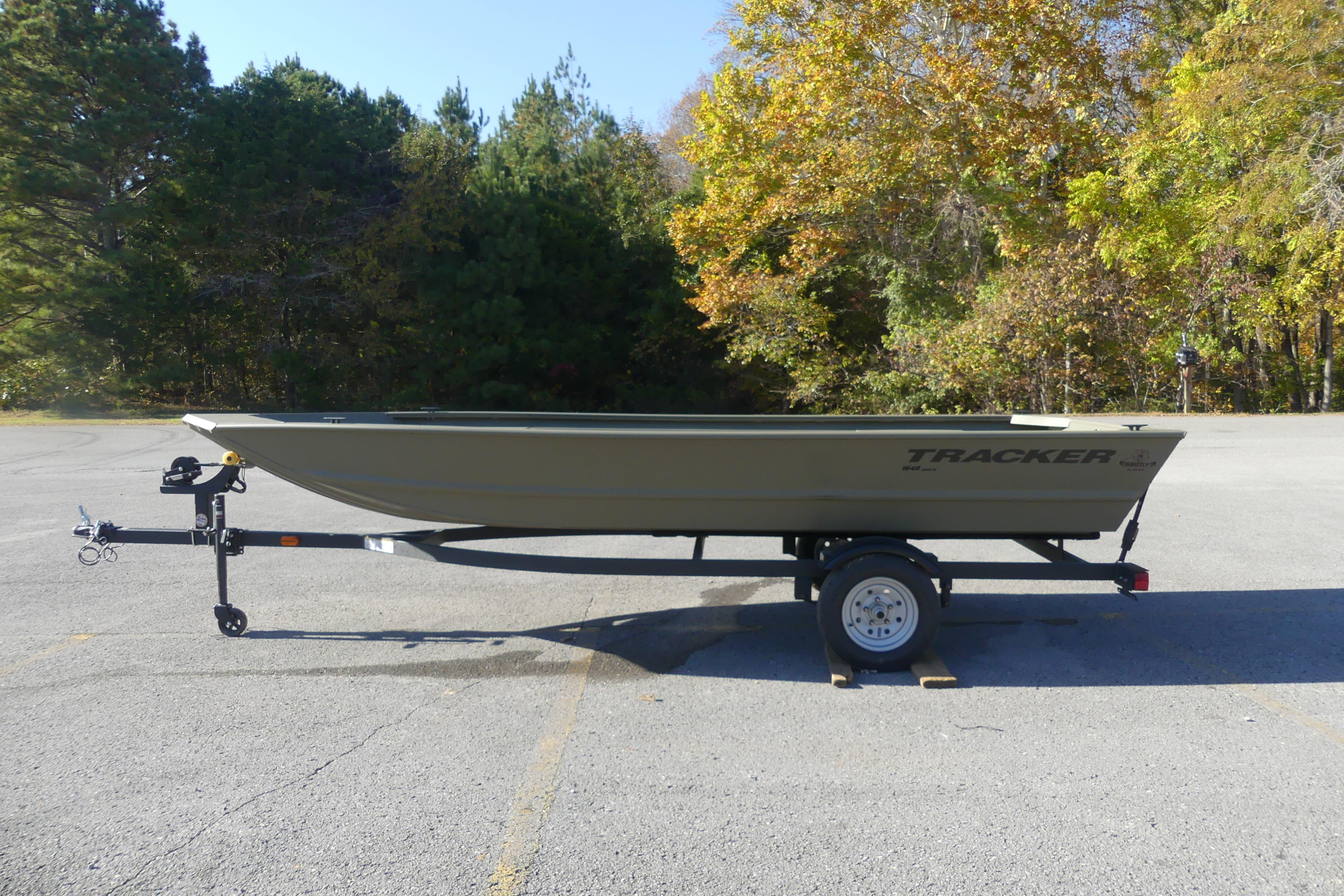 2026 Tracker Grizzly 1648 Utility boat on trailer in a parking lot, surrounded by trees.