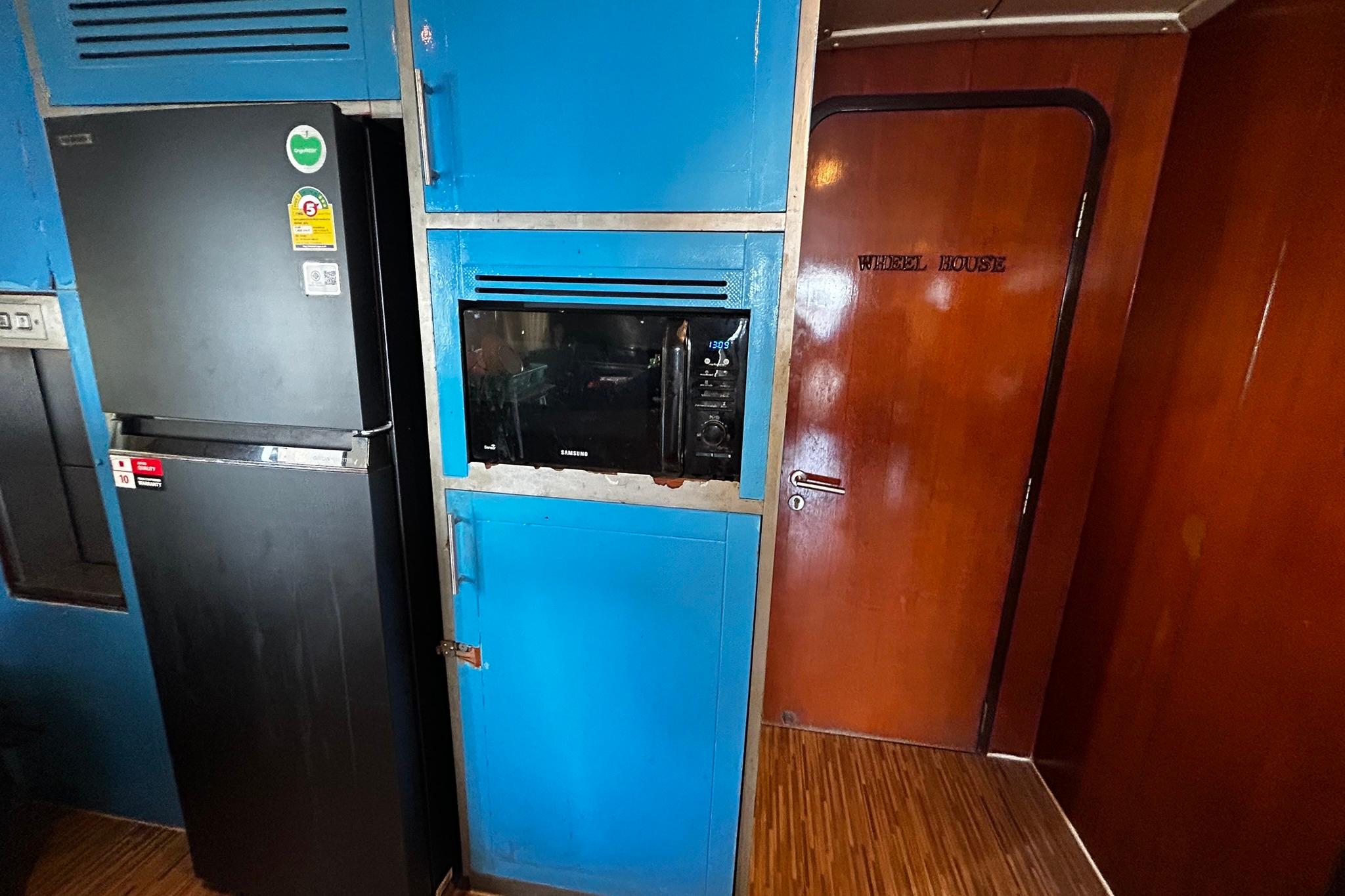 Kitchen area with blue cabinets, black fridge, microwave, and "Wheel House" door, Custom 28M, 1999.