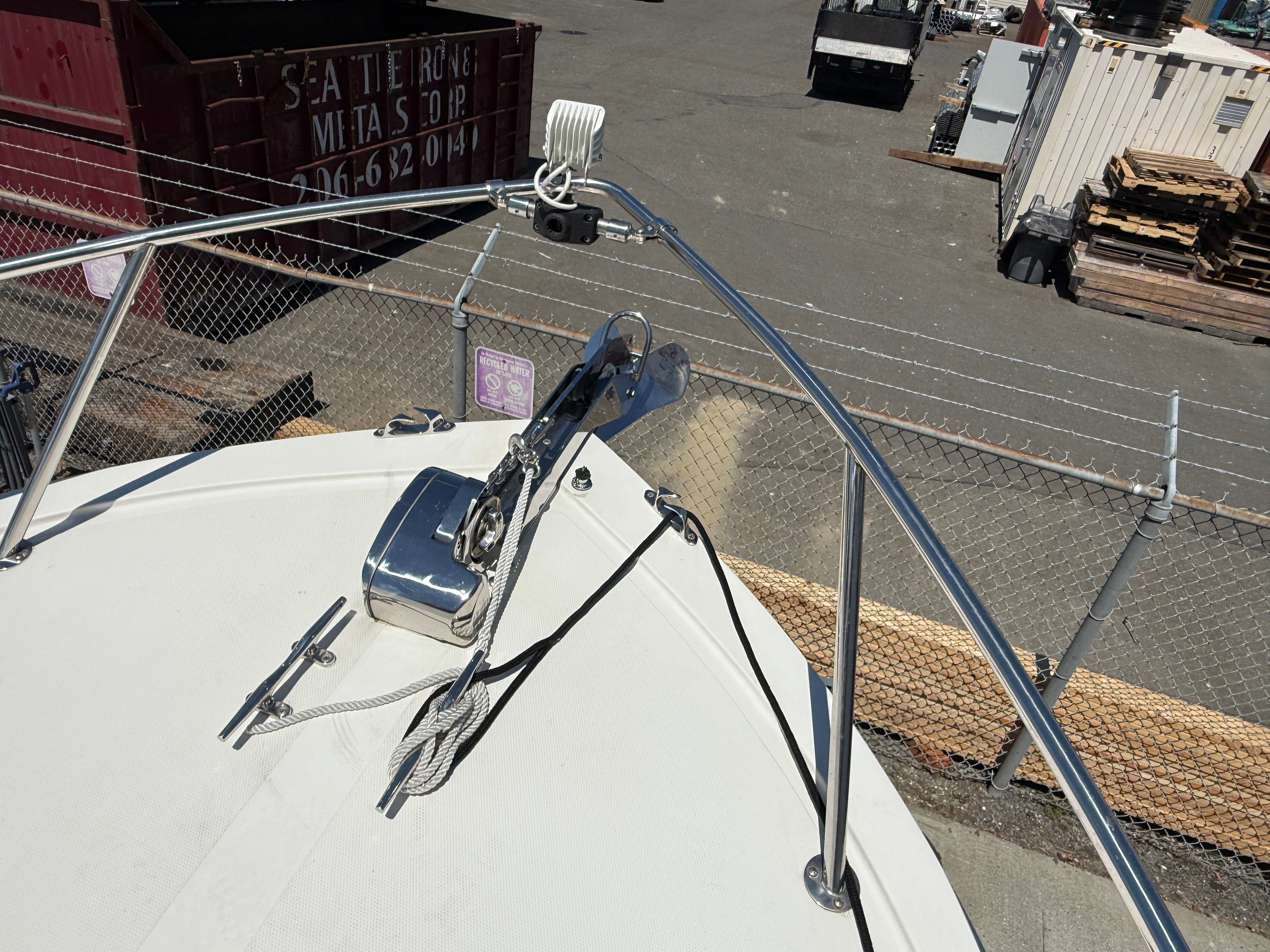 Boat's foredeck with anchor windlass and rope, surrounded by a metal fence.