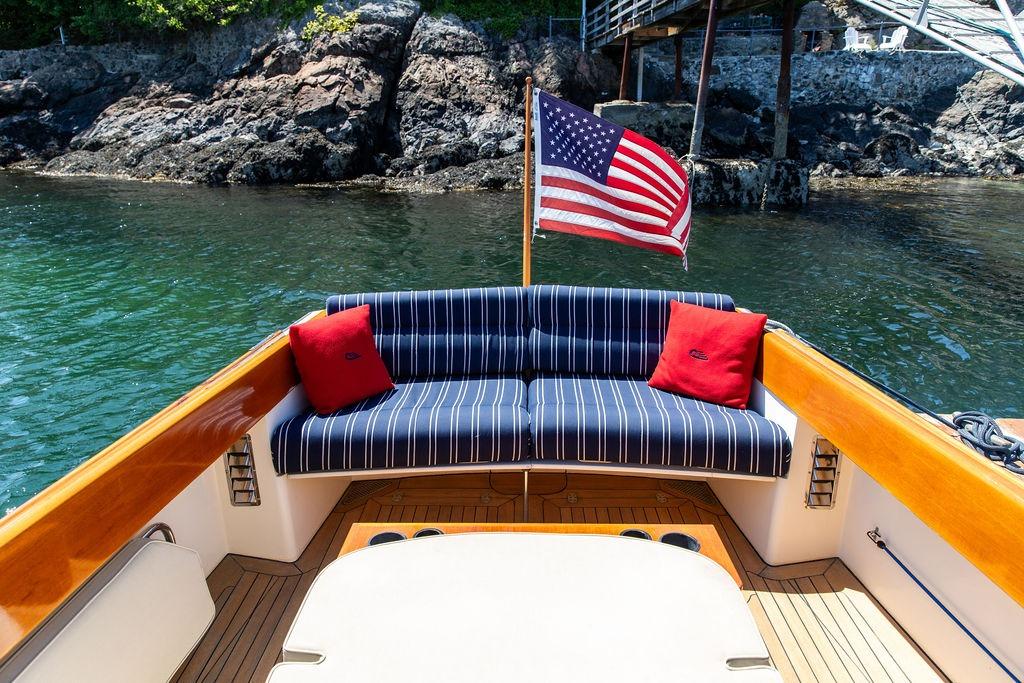 Hinckley Picnic Boat 36 Classic, 2000 model, with striped seating and American flag, near rocky shoreline.