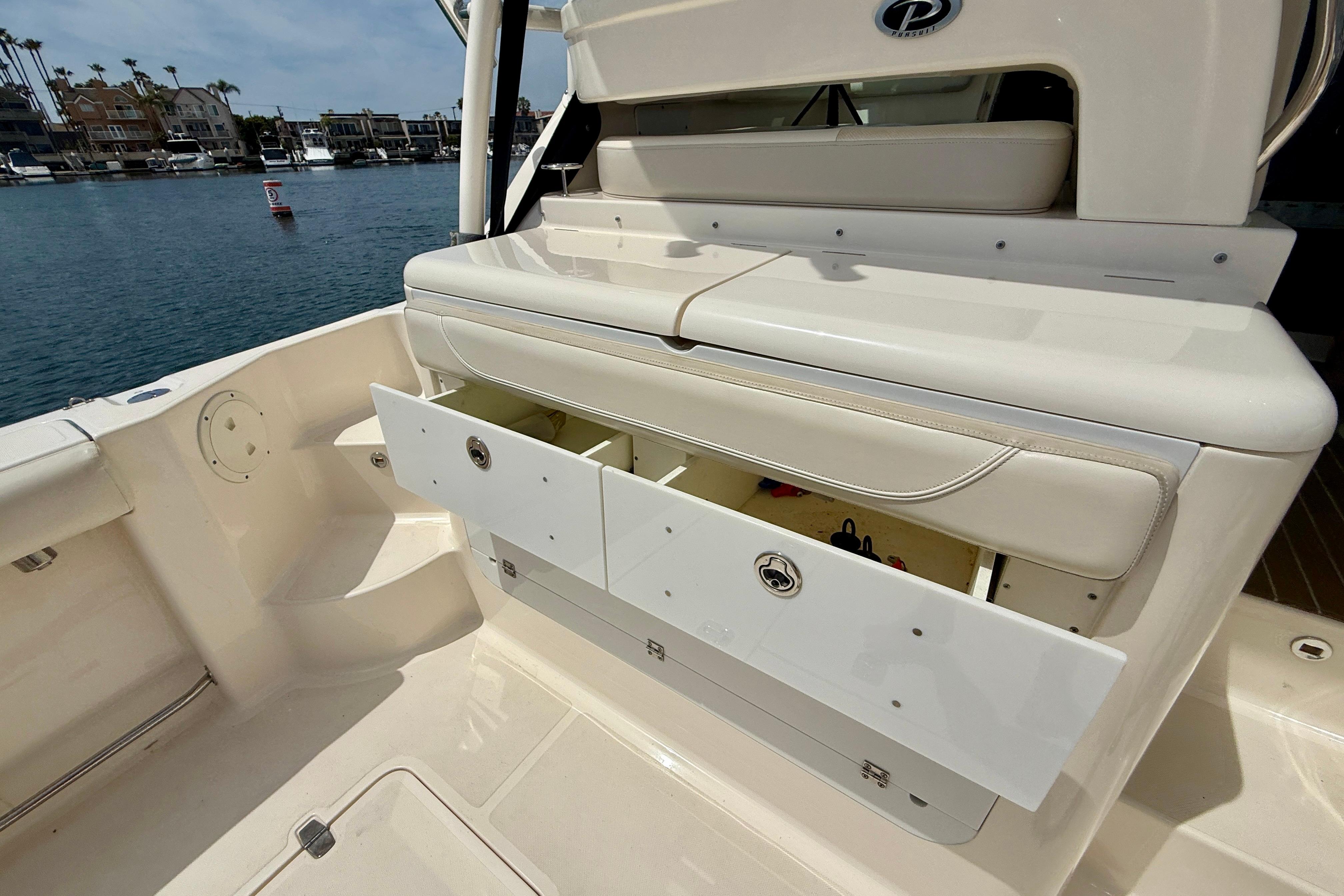 2012 Pursuit OS 345 Offshore boat with open storage compartments, docked by waterfront homes.