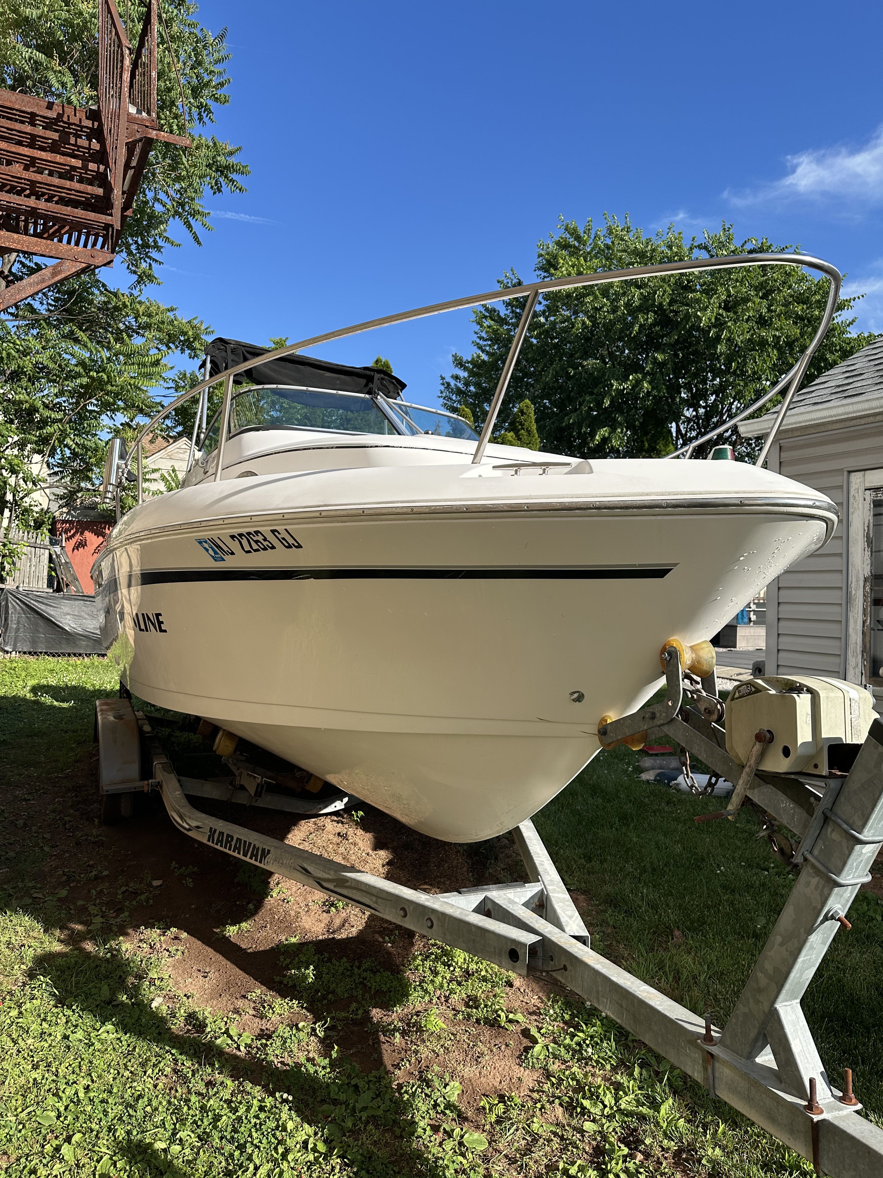 A 1999 Pro-Line 221 boat on a trailer outdoors, surrounded by trees.