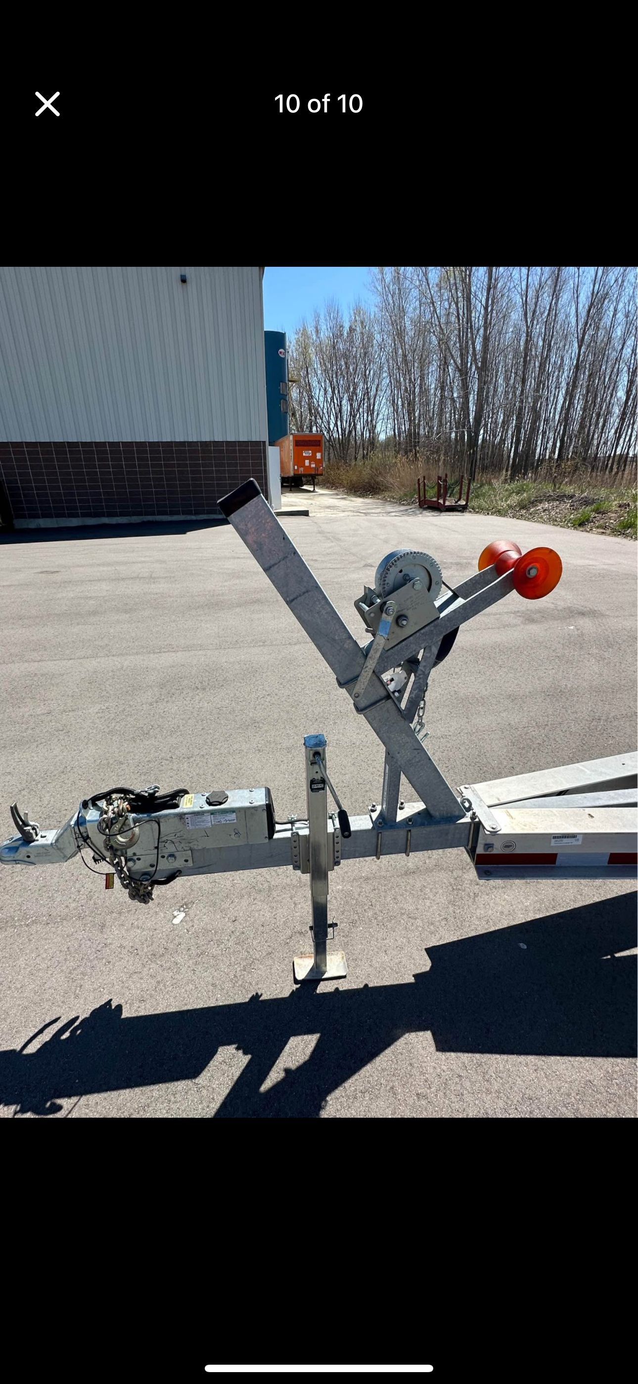 A boat trailer with a winch and orange roller holder is parked on a lot.
