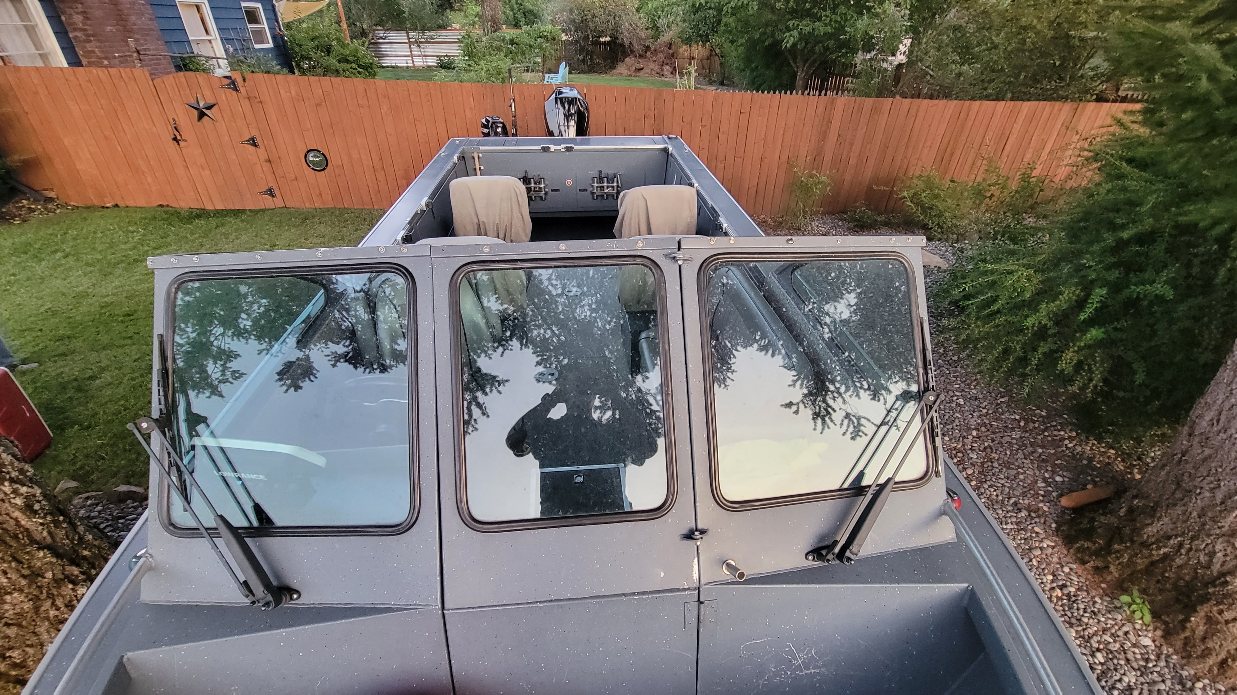 A 2015 Alumaweld Formula Vee Outboard 24 is parked in a garden with a wooden fence.