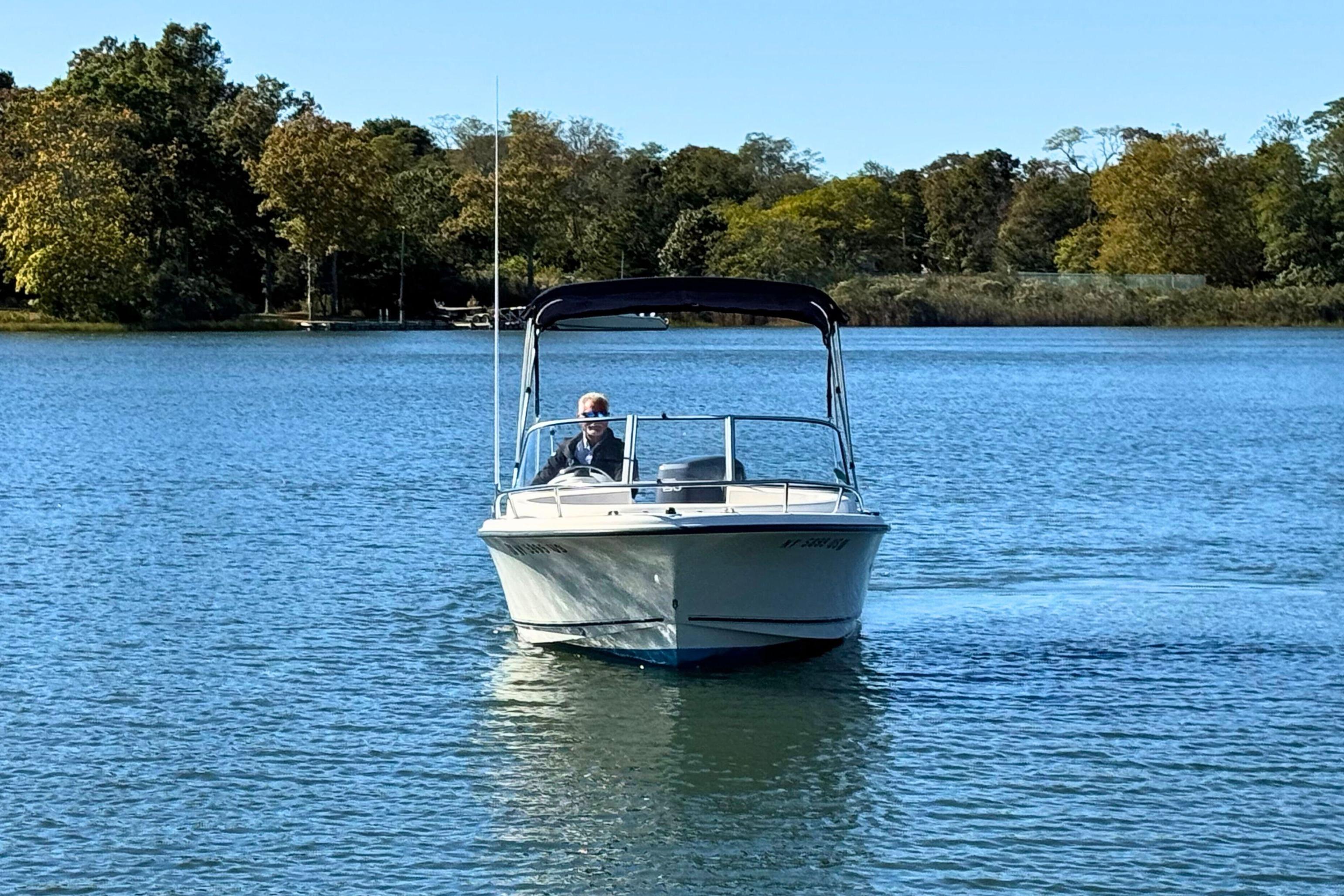 2002 Sea Hunt Escape 200 boat cruising on a serene lake with lush green trees.