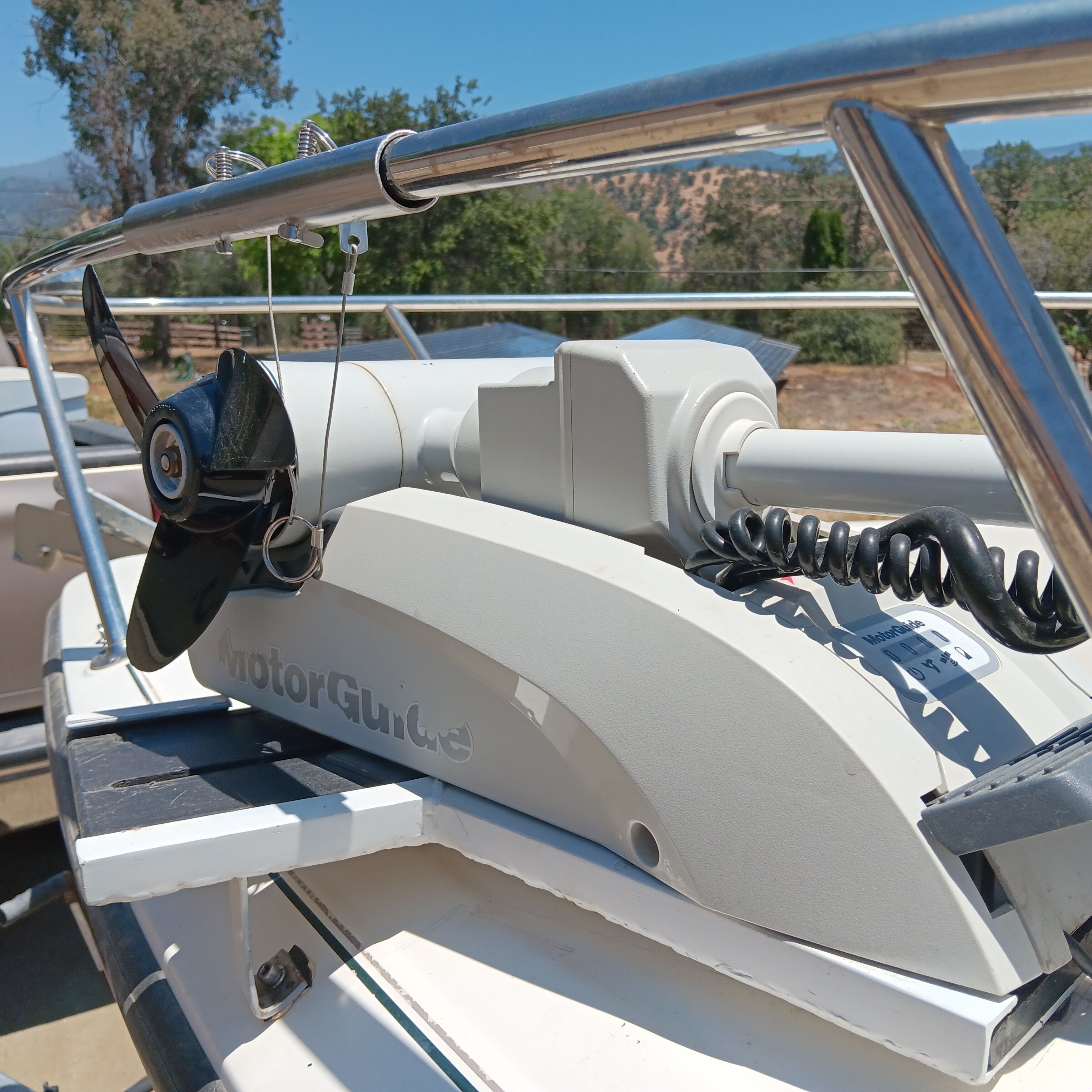 A MotorGuide motor is mounted on a boat, surrounded by trees and clear sky.