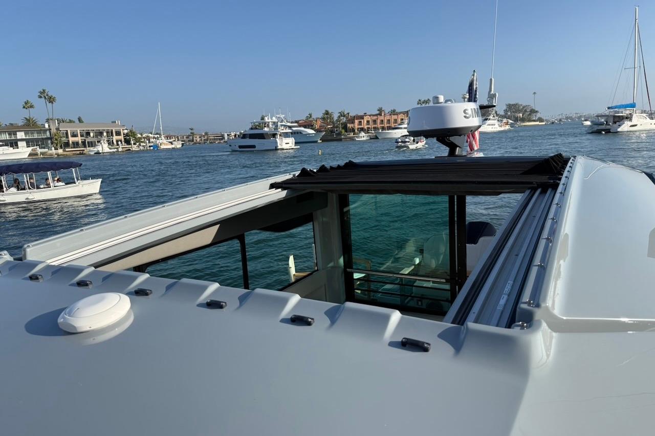 2024 Saxdor 320 GTC yacht with open sunroof, cruising in a scenic harbor.