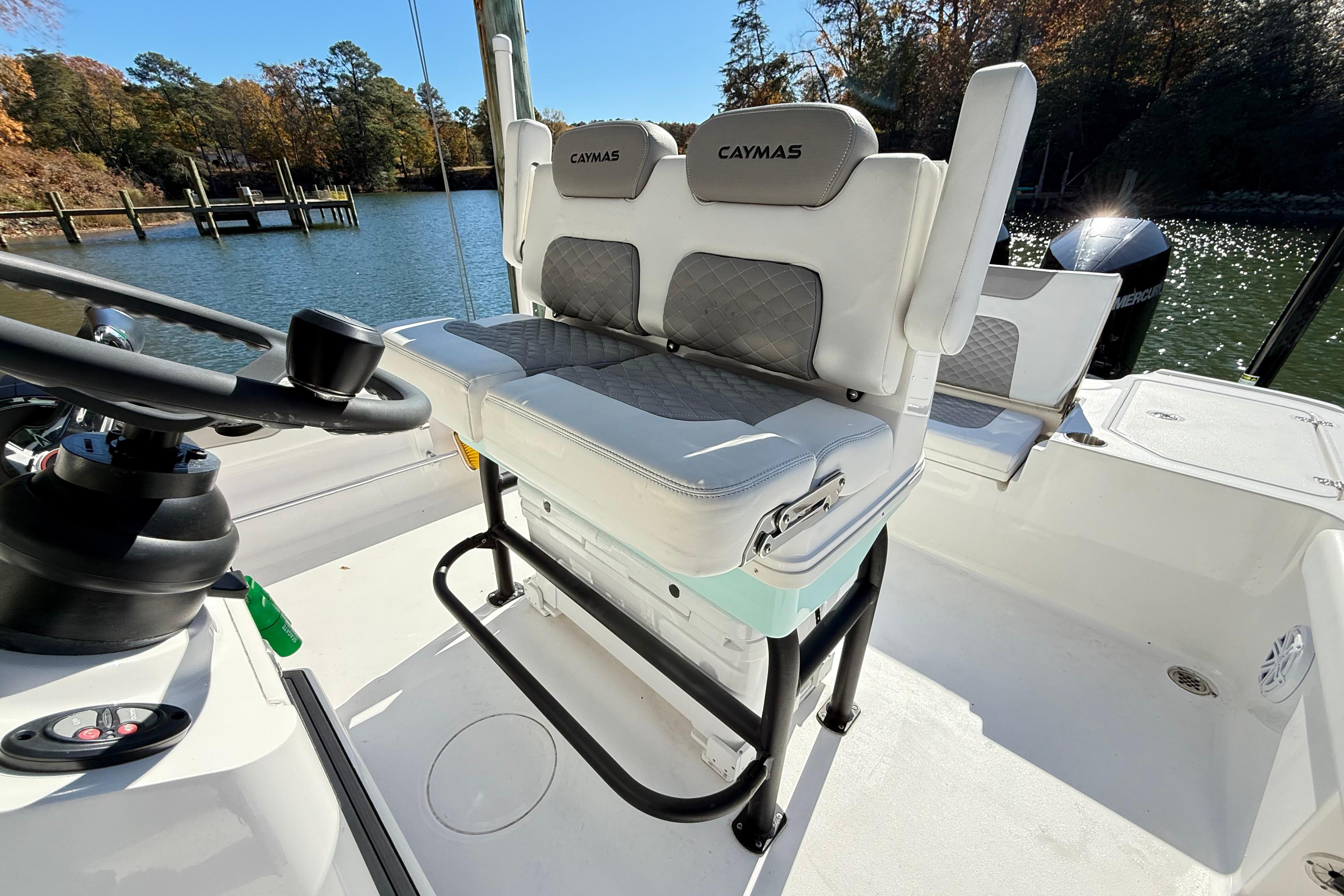2023 Caymas 281 HB boat interior with cushioned seating and steering wheel, docked by a scenic lake.