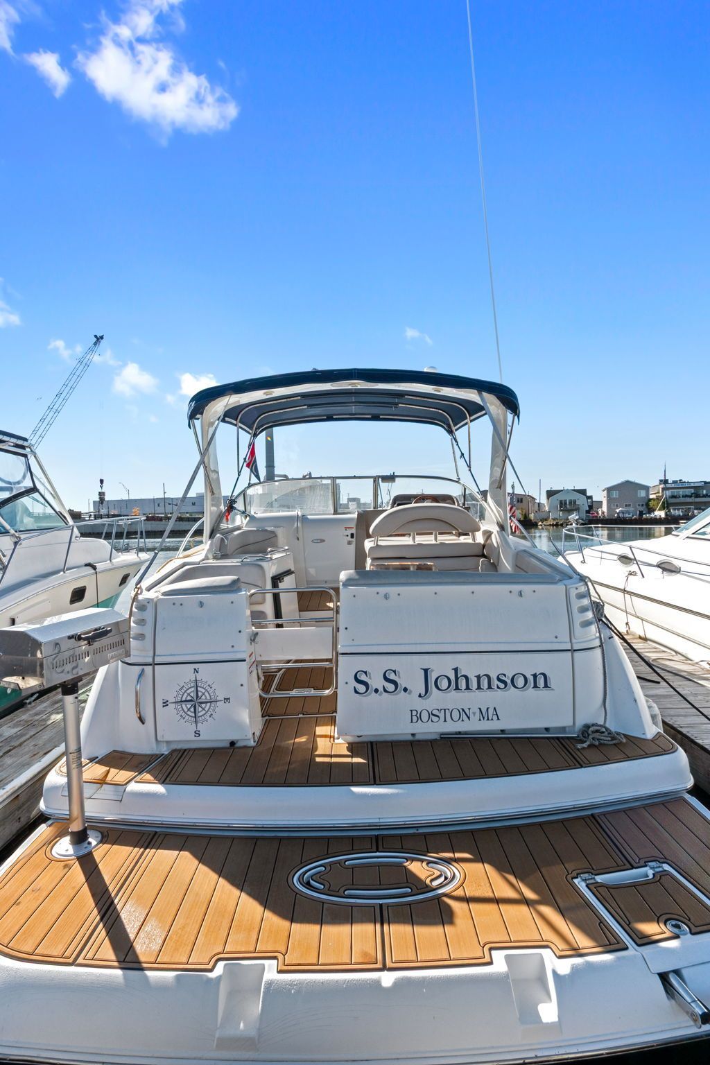 A 2007 Larson Cabrio 330 with wooden deck, seating, and blue canopy docked in a harbor.