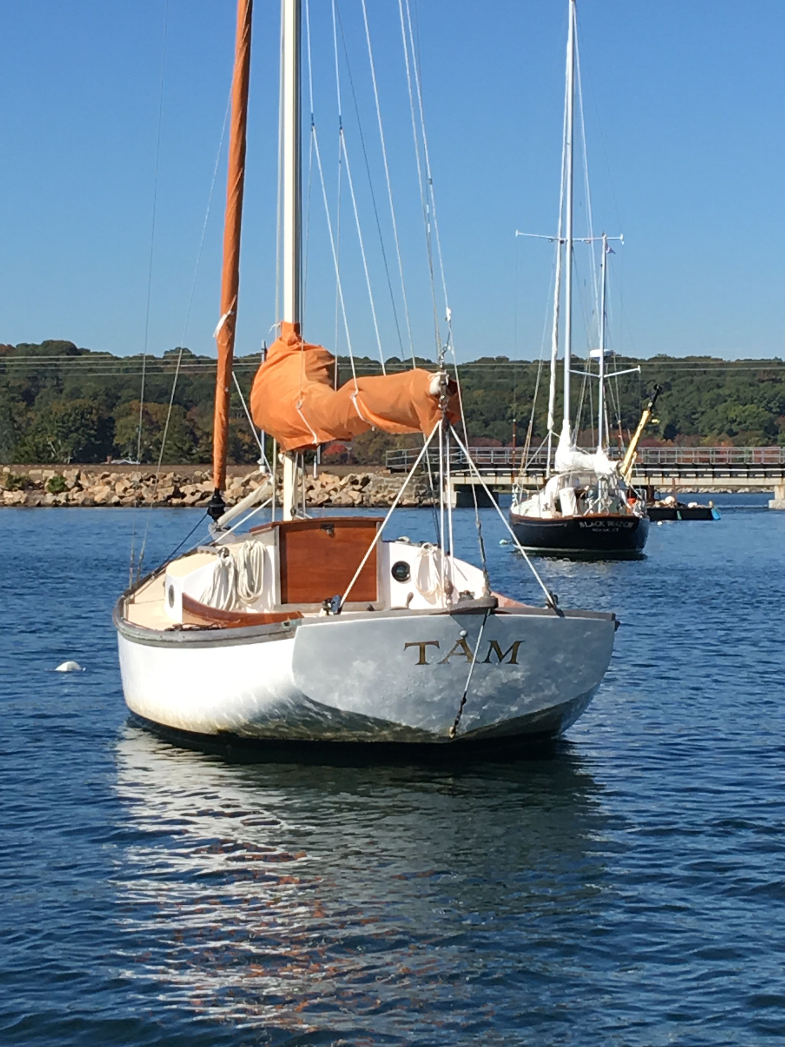 A white sailboat with an orange sail is anchored on calm water.