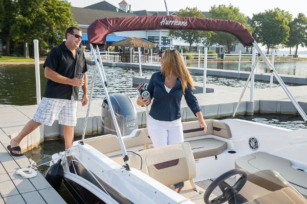 Couple enjoying a 2025 Hurricane SunDeck Sport 205 OB boat at a scenic dock.