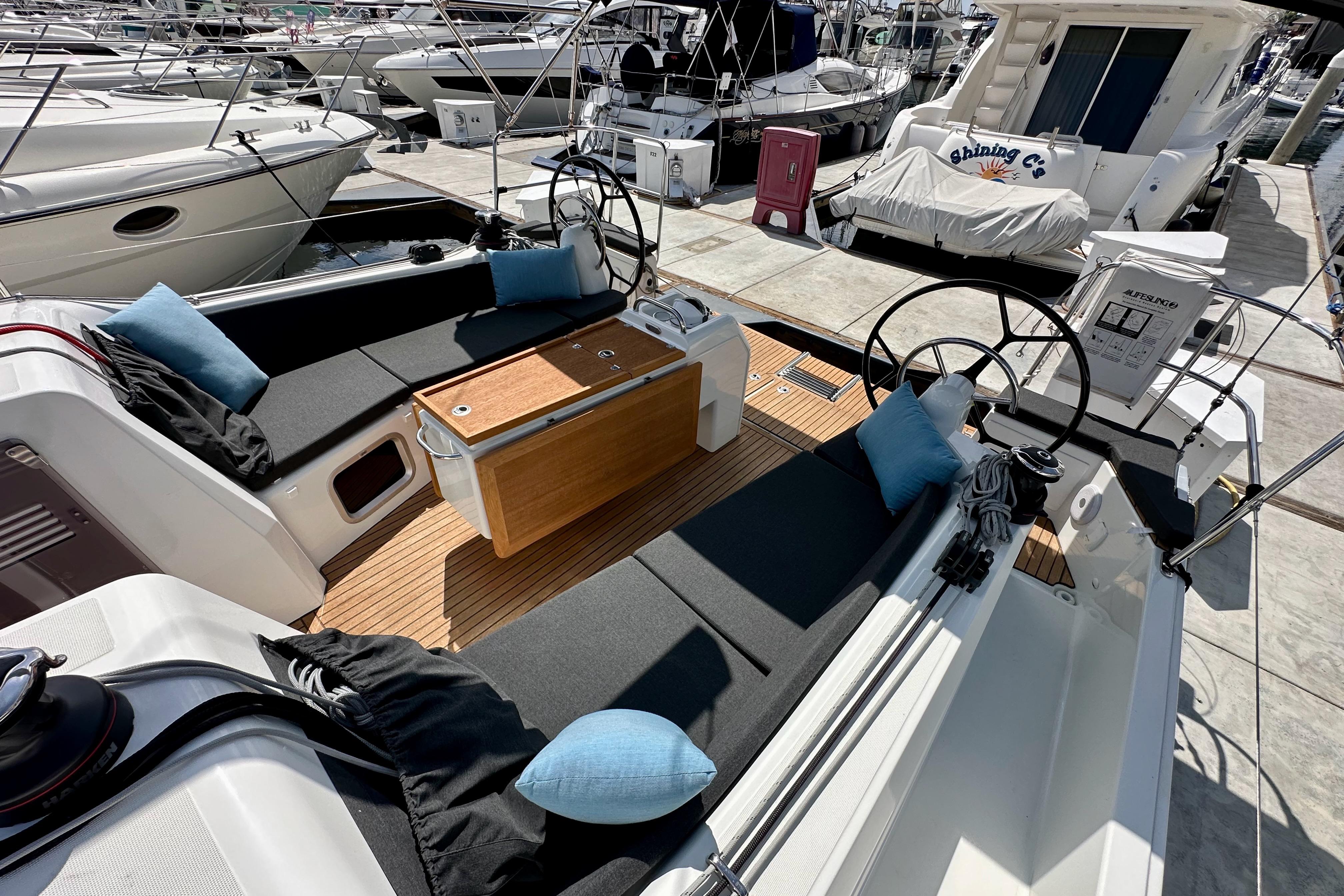 2024 Jeanneau Sun Odyssey 410 yacht cockpit with seating, cushions, and steering wheels at a marina.
