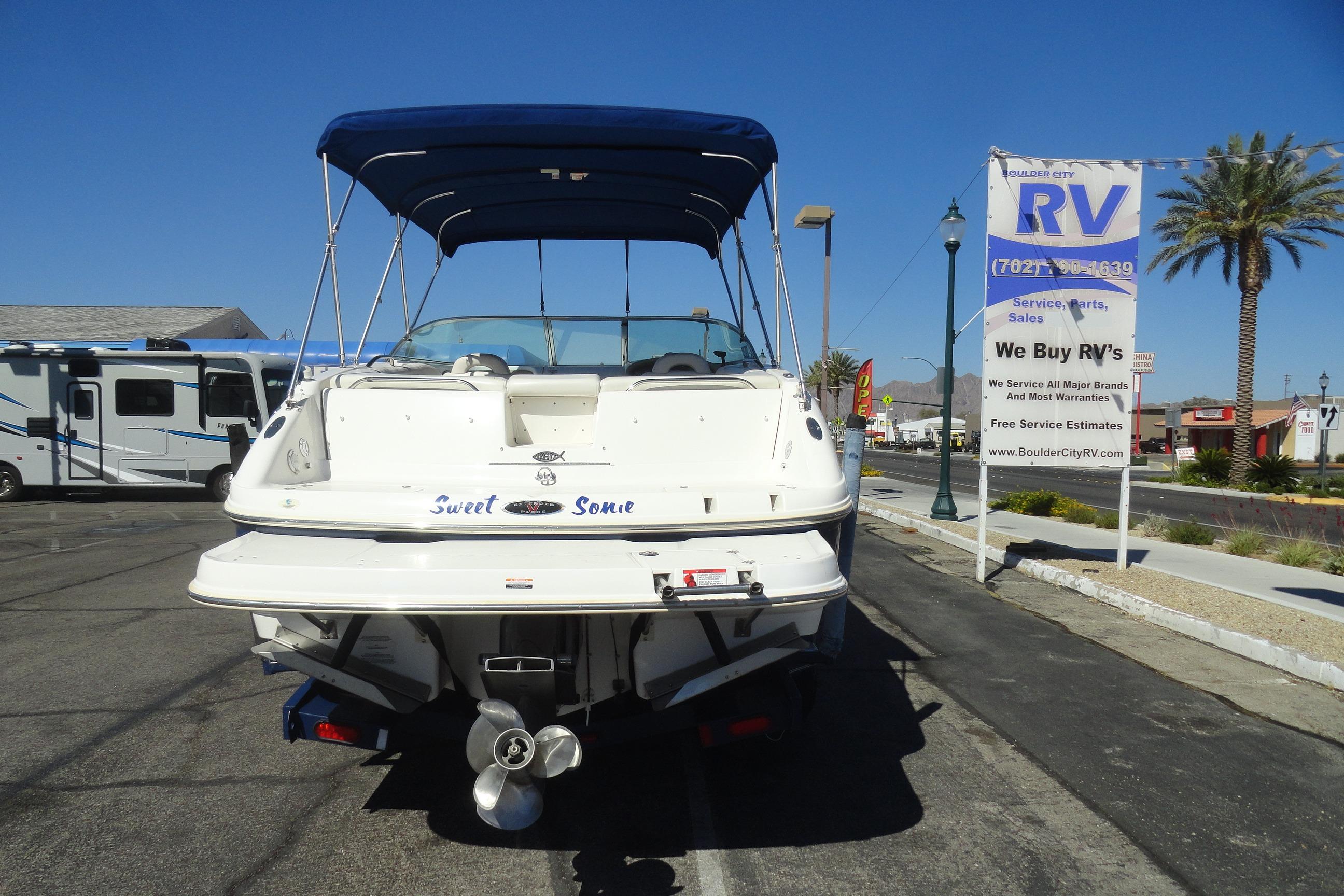 2001 Chaparral 265 SSi boat with blue canopy, parked near RV dealership sign.
