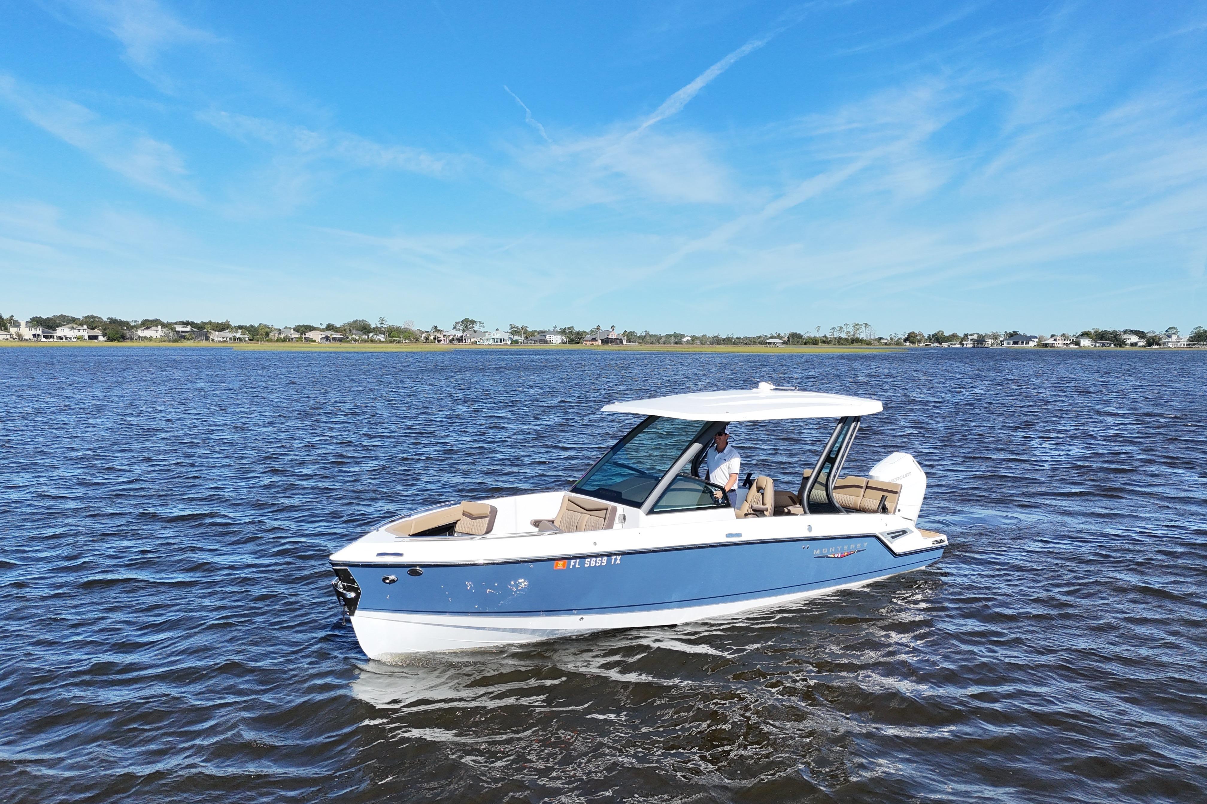 2025 Monterey Elite 27 OB boat cruising on a calm lake under a clear blue sky.