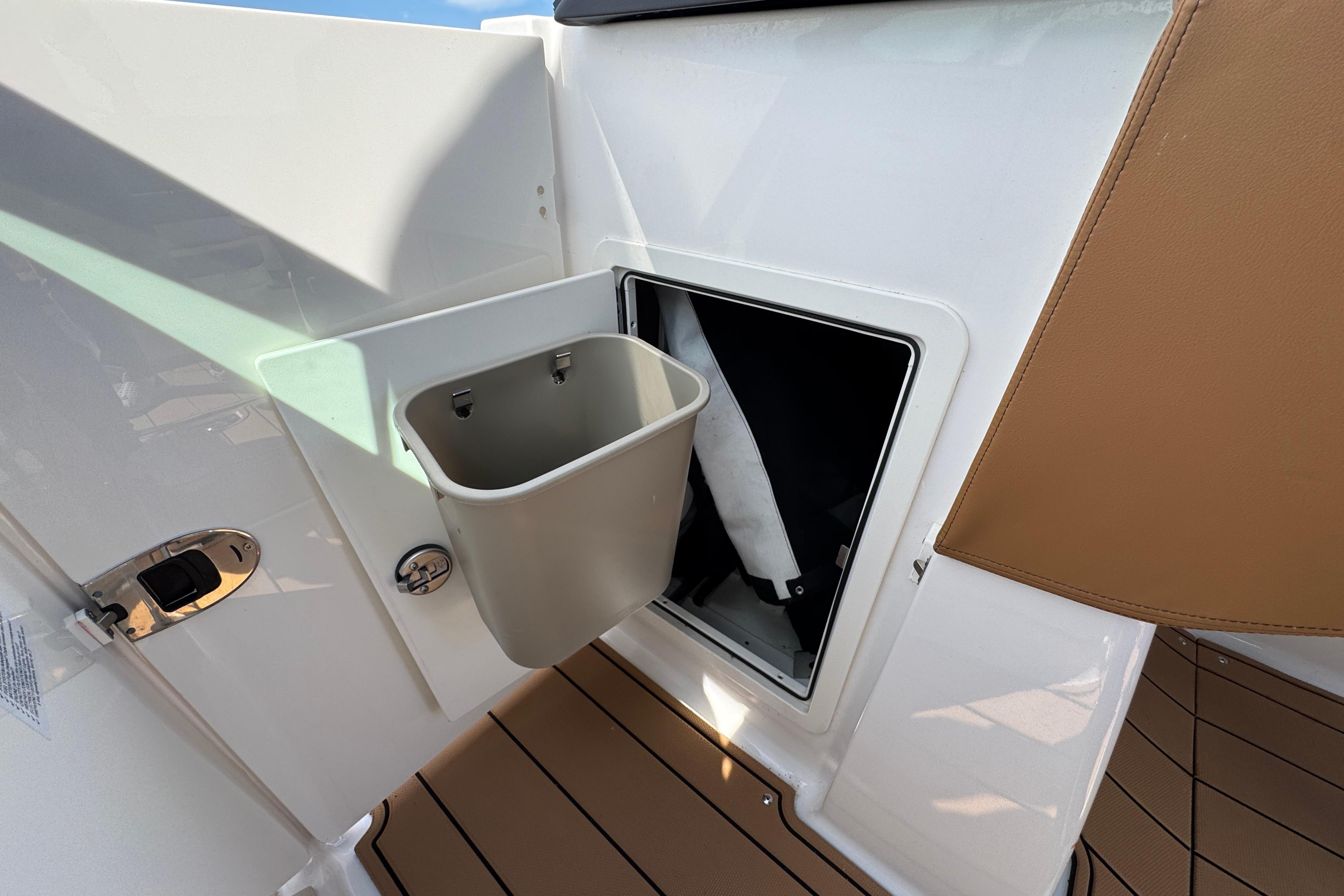 2023 Chaparral 26 Surf boat interior with built-in storage compartment and trash bin.