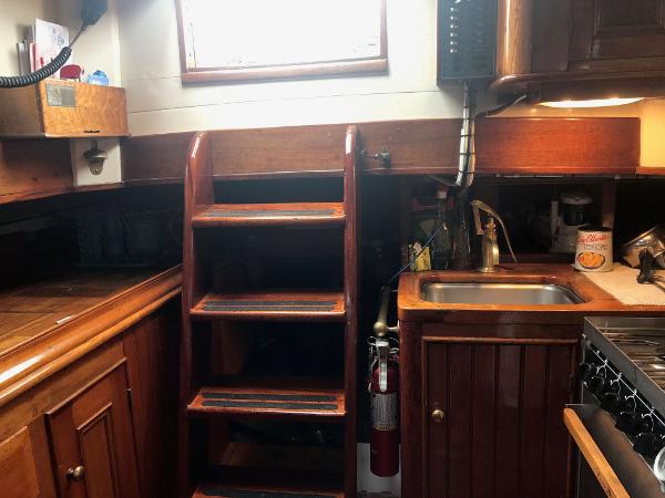 1983 Custom Murray Peterson Coaster III yacht interior with wooden cabinetry, sink, and ladder.