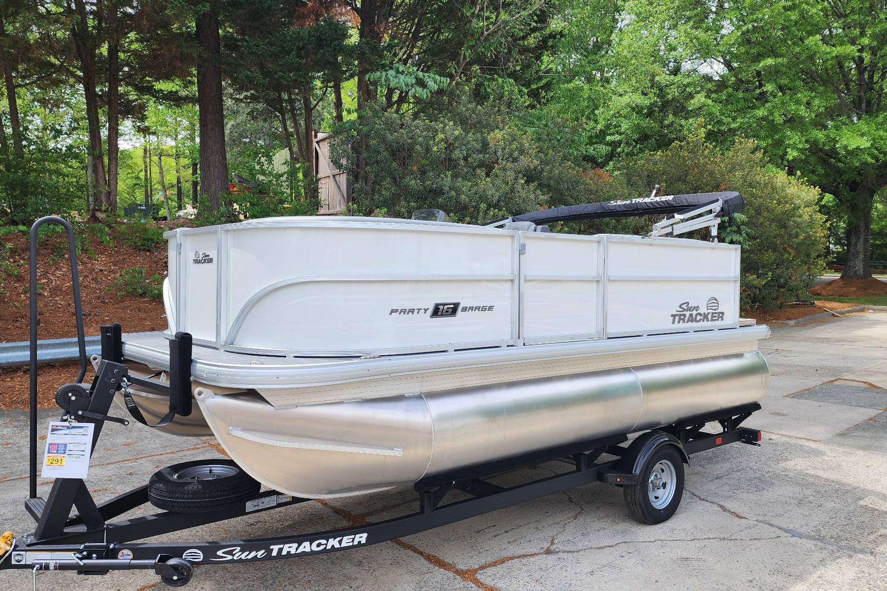 2026 Sun Tracker Party Barge 16 DLX pontoon boat on trailer, surrounded by trees.