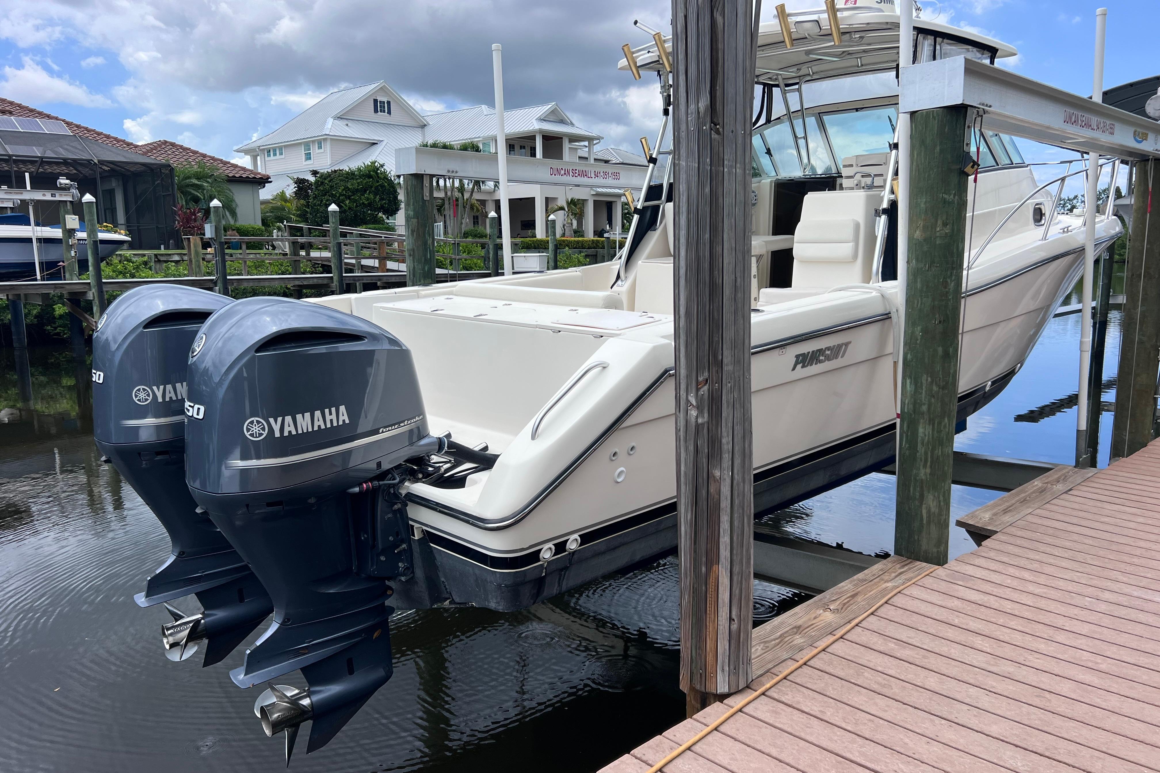 2005 Pursuit 3070 Offshore boat with twin Yamaha engines docked by waterfront homes.