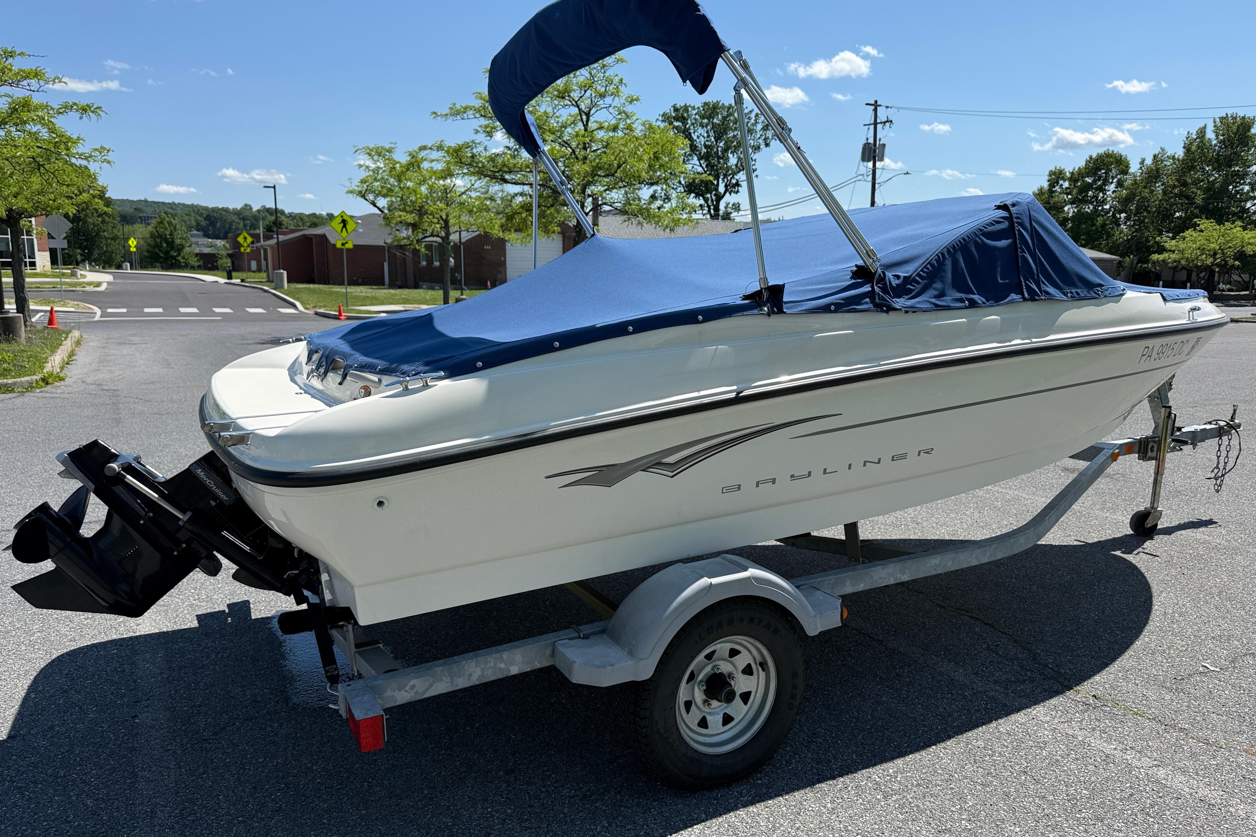 2009 Bayliner 175 boat on trailer with blue cover, parked outdoors on sunny day.
