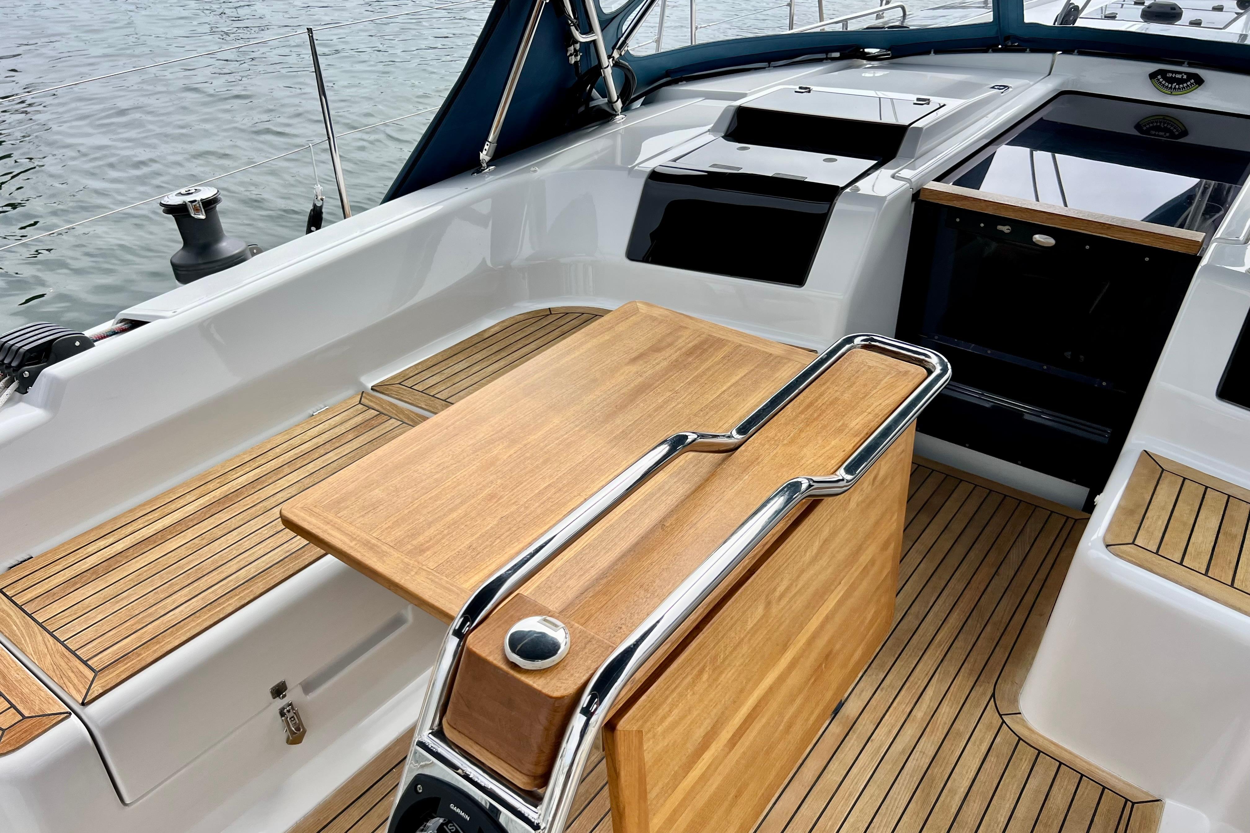 Cockpit of 2016 Hanse 455 yacht with wooden table and seating, docked by water.
