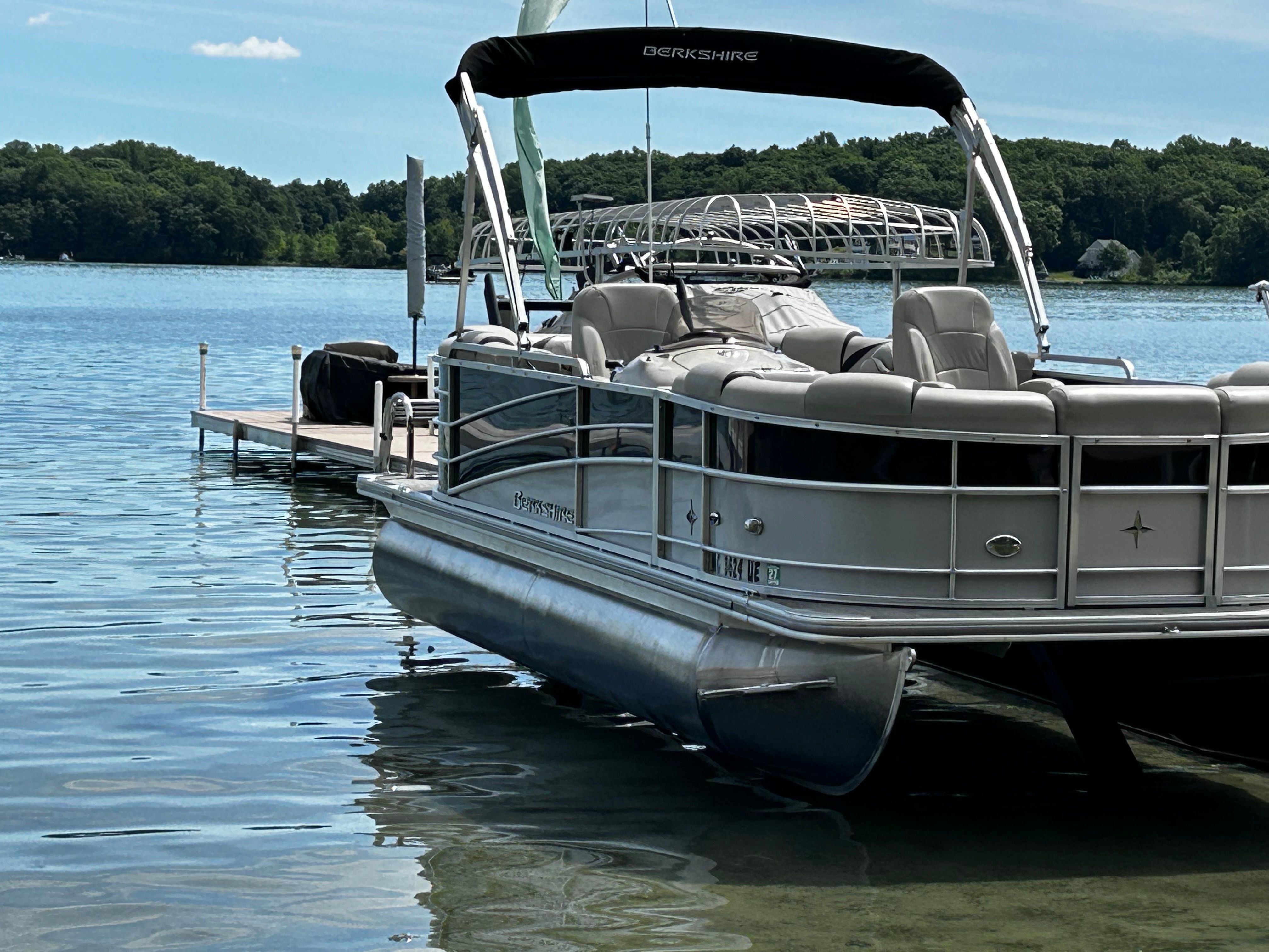 A pontoon boat is docked at a pier on a calm lake.