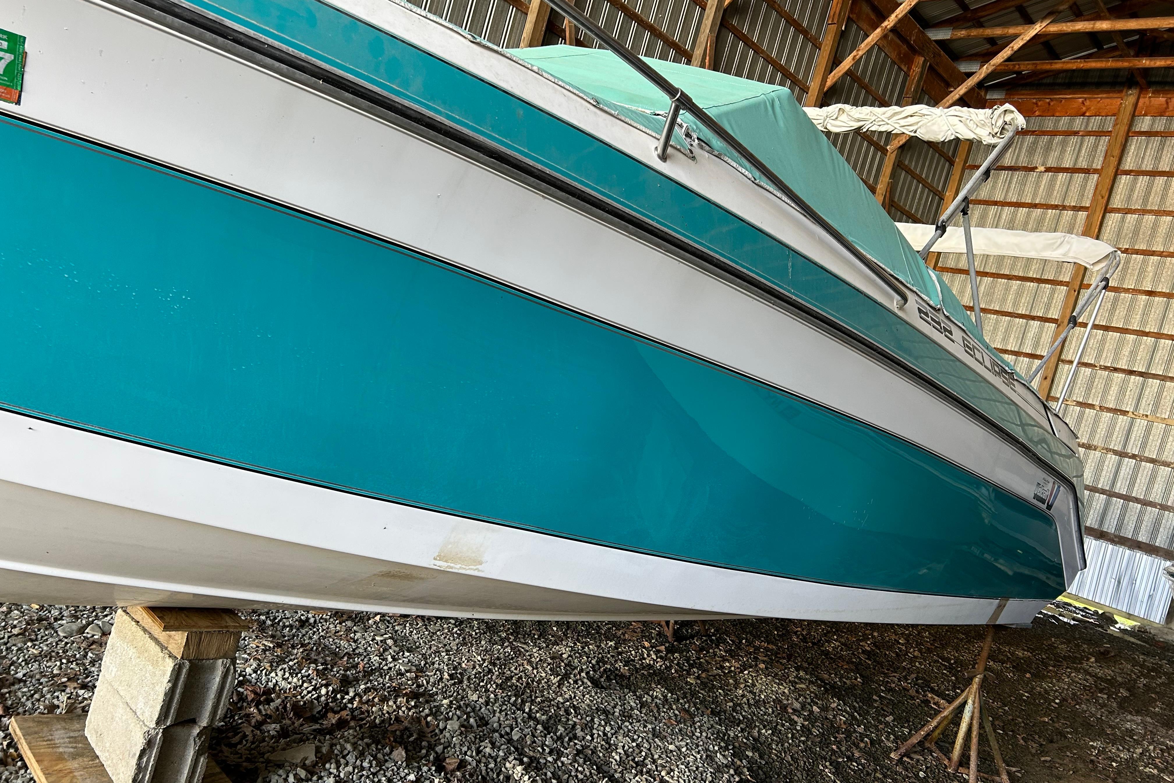 1991 Wellcraft 232 Eclipse boat in storage, teal and white exterior, supported on blocks.